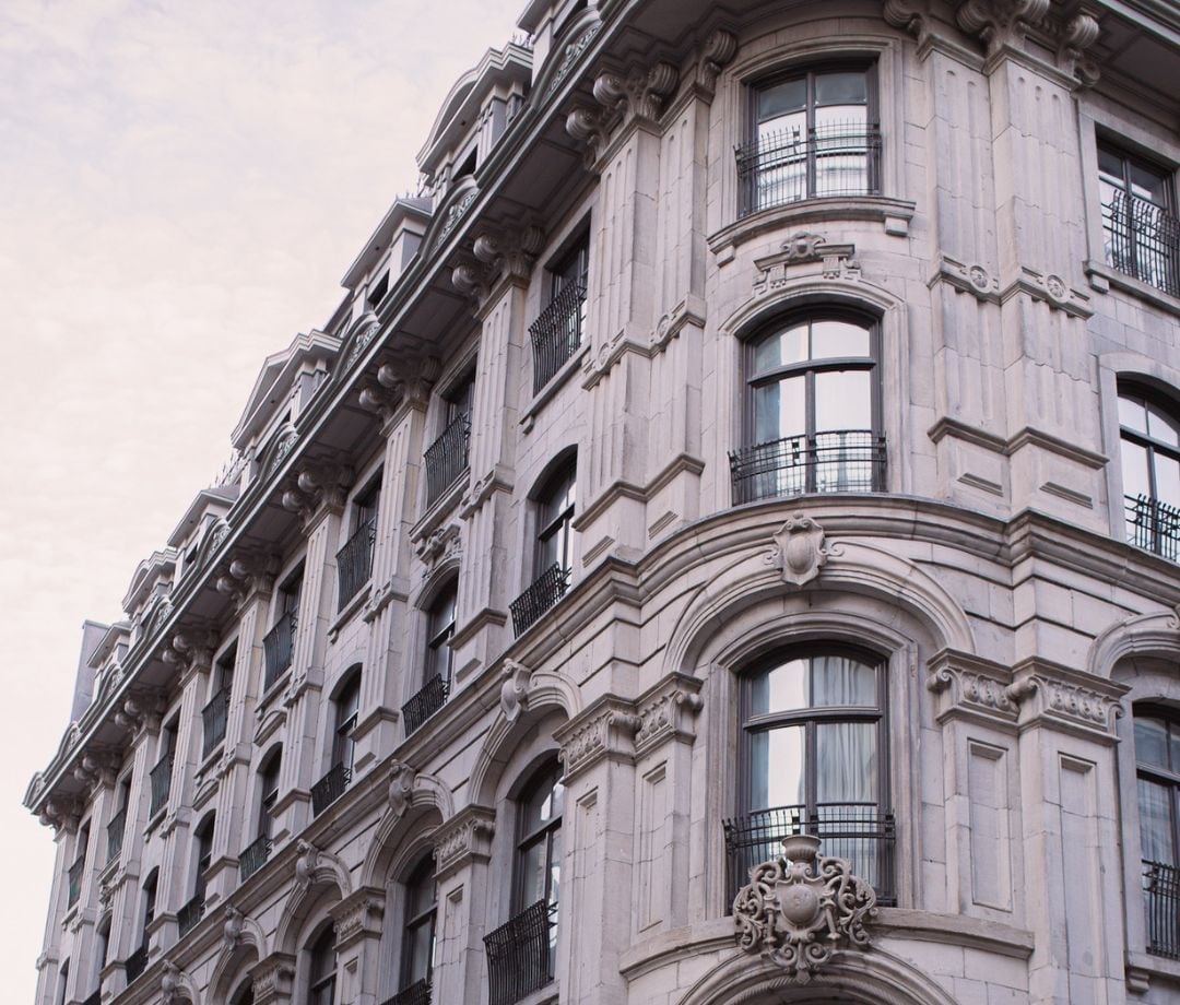 Ornate Haussmanian stonework and wrought-iron balconies define this elegant corner facade, where classical French architecture meets modern boutique hospitality in Old Montreal's cobblestone district.
