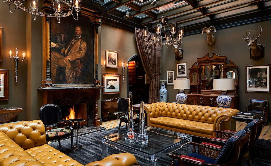 Leather Chesterfields and taxidermy create an intimate gentleman's club atmosphere in this richly appointed lounge, where flickering firelight dances across oil paintings and coffered ceilings.