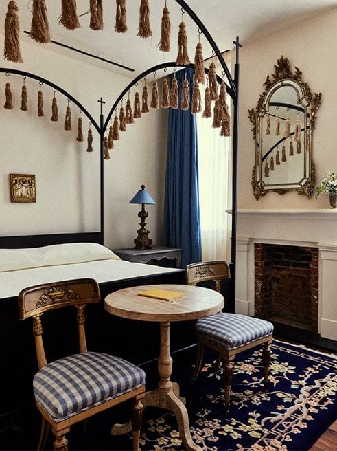 Wrought-iron canopy beds draped with bronze tassels create intimate sanctuaries, while gingham-cushioned chairs and ornate mirrors evoke New Orleans' historic French Quarter charm.