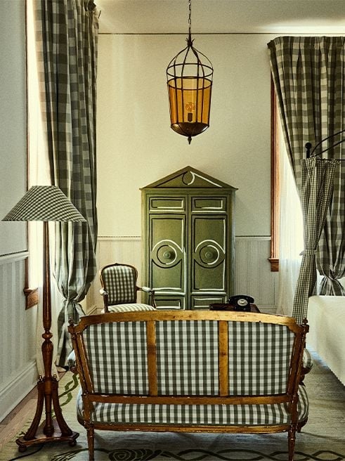 Gingham fabrics and sage-green armoires create cottage charm in this thoughtfully appointed guest room, where amber lantern light casts golden shadows across vintage furnishings.