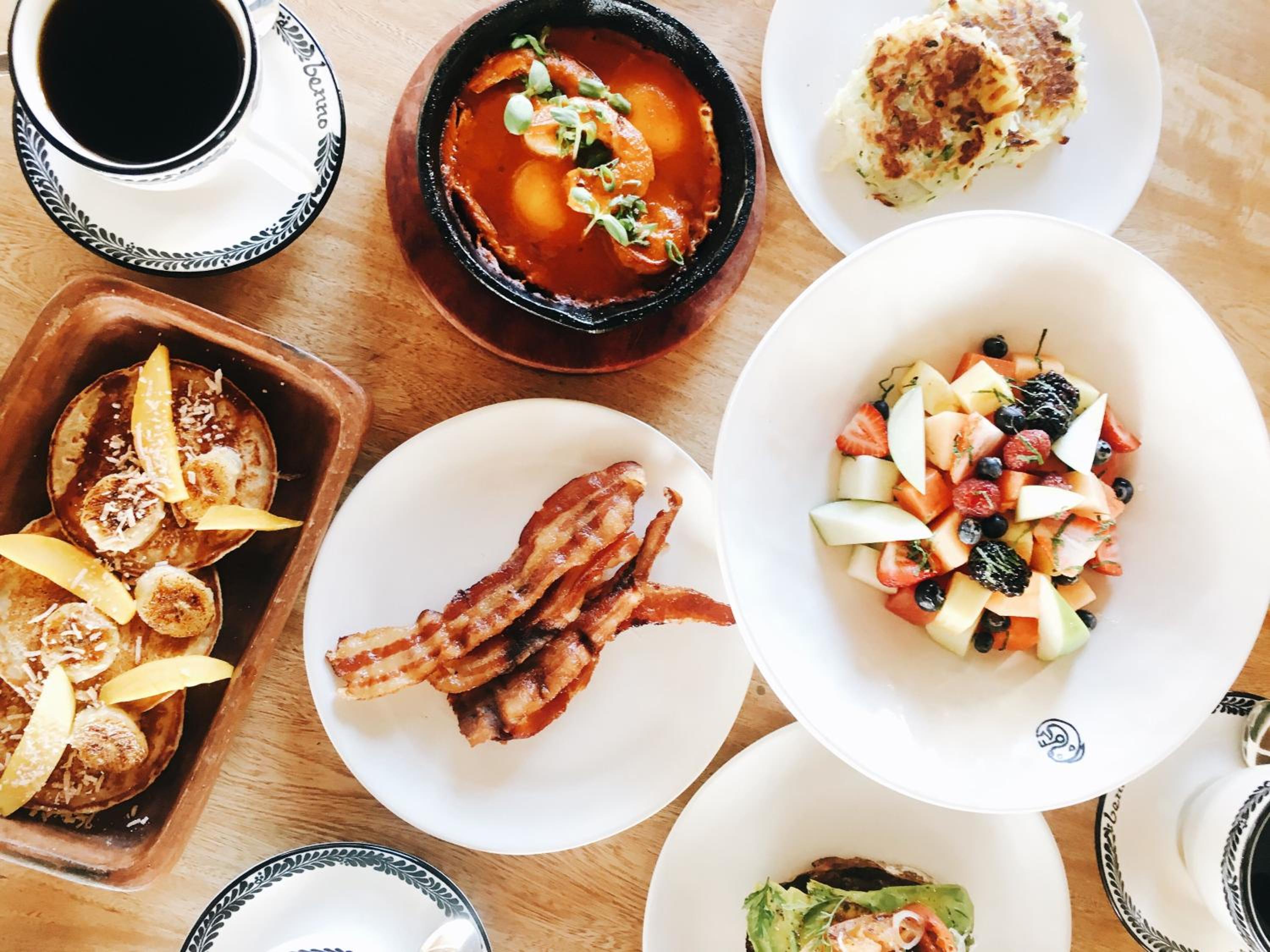 Fresh-caught shrimp sizzle in clay pots while crispy bacon and colorful salads create a vibrant breakfast spread that captures Baja's farm-to-table spirit.