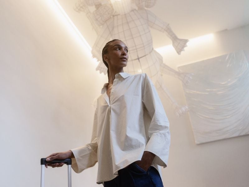 Sunlight streams through Hotel St. George's soaring atrium as a guest moves through the minimalist white lobby, her flowing shirt catching the ethereal glow.