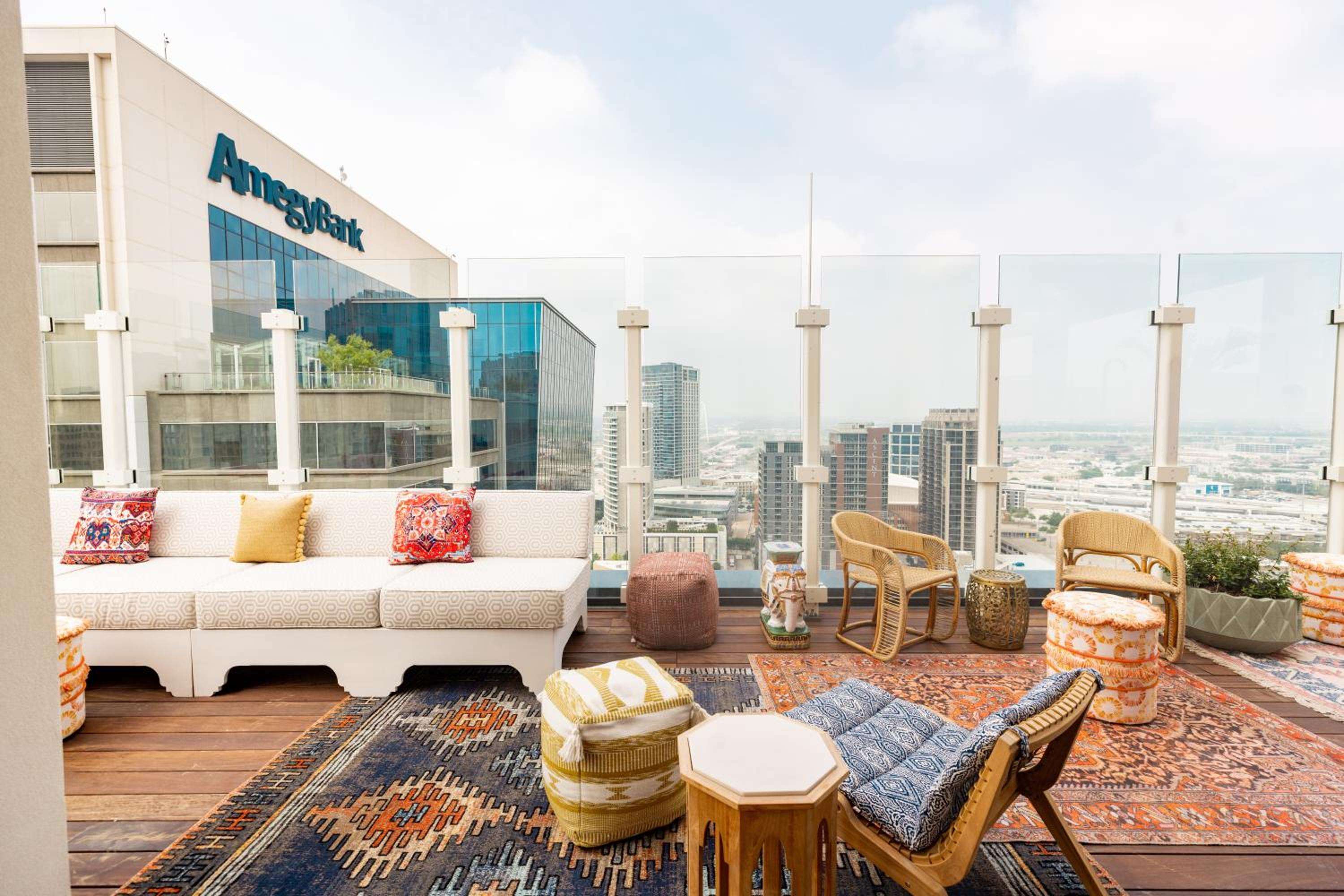 Vibrant kilim rugs and woven rattan chairs create an inviting rooftop sanctuary, where Dallas skyline views stretch beyond glass windscreens and colorful cushions beckon long conversations.