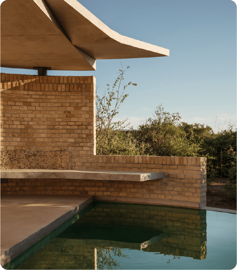 Warm brick and curved concrete create intimate poolside moments, where golden hour light dances across mosaic tiles and still water mirrors the desert sky.