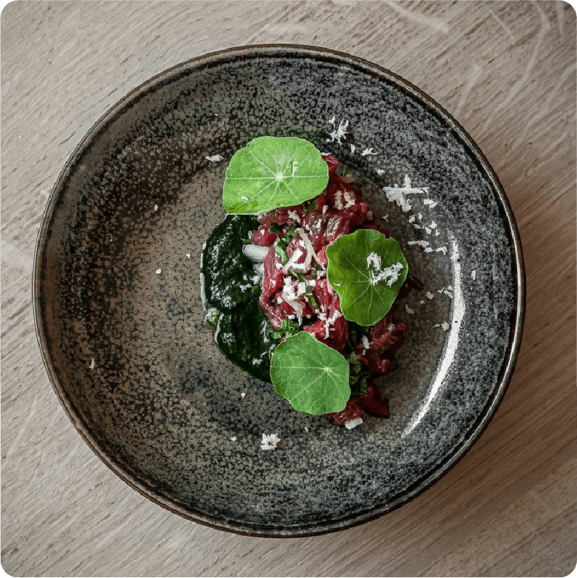 Raw beef tartare glistens with fresh herbs and nasturtium leaves in this artfully composed dish, showcasing the kitchen's commitment to seasonal, locally-sourced ingredients.