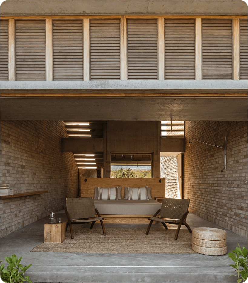 Raw brick walls frame a sculptural bathtub beneath wooden shutters, where industrial minimalism meets tropical warmth in this striking open-plan suite.