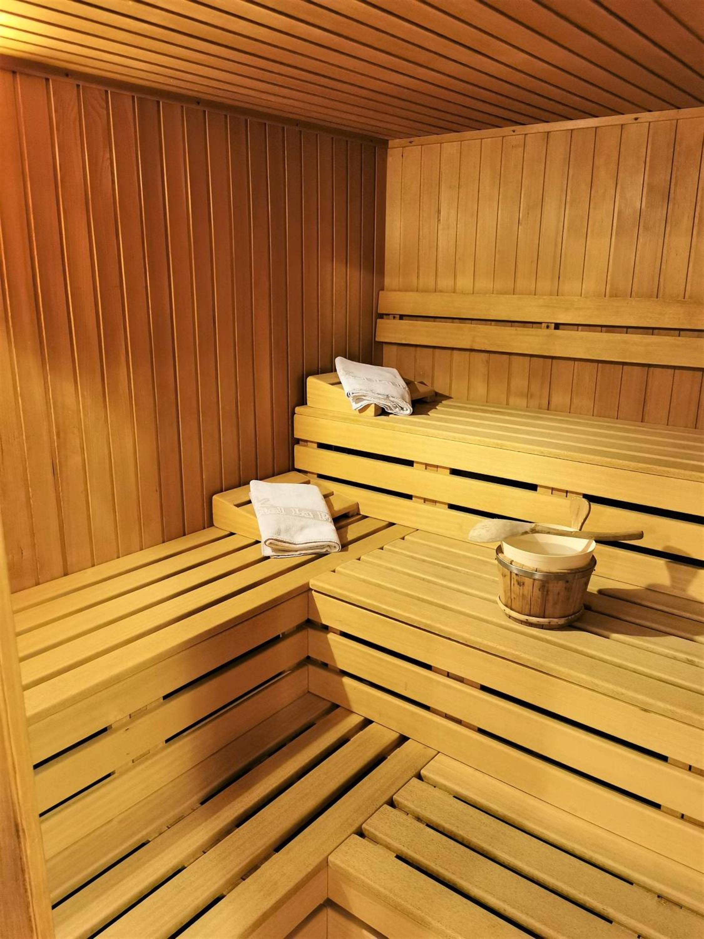 Warm cedar envelops guests in the hotel's Finnish sauna, where wooden buckets and crisp linens await amid the golden glow of therapeutic heat.