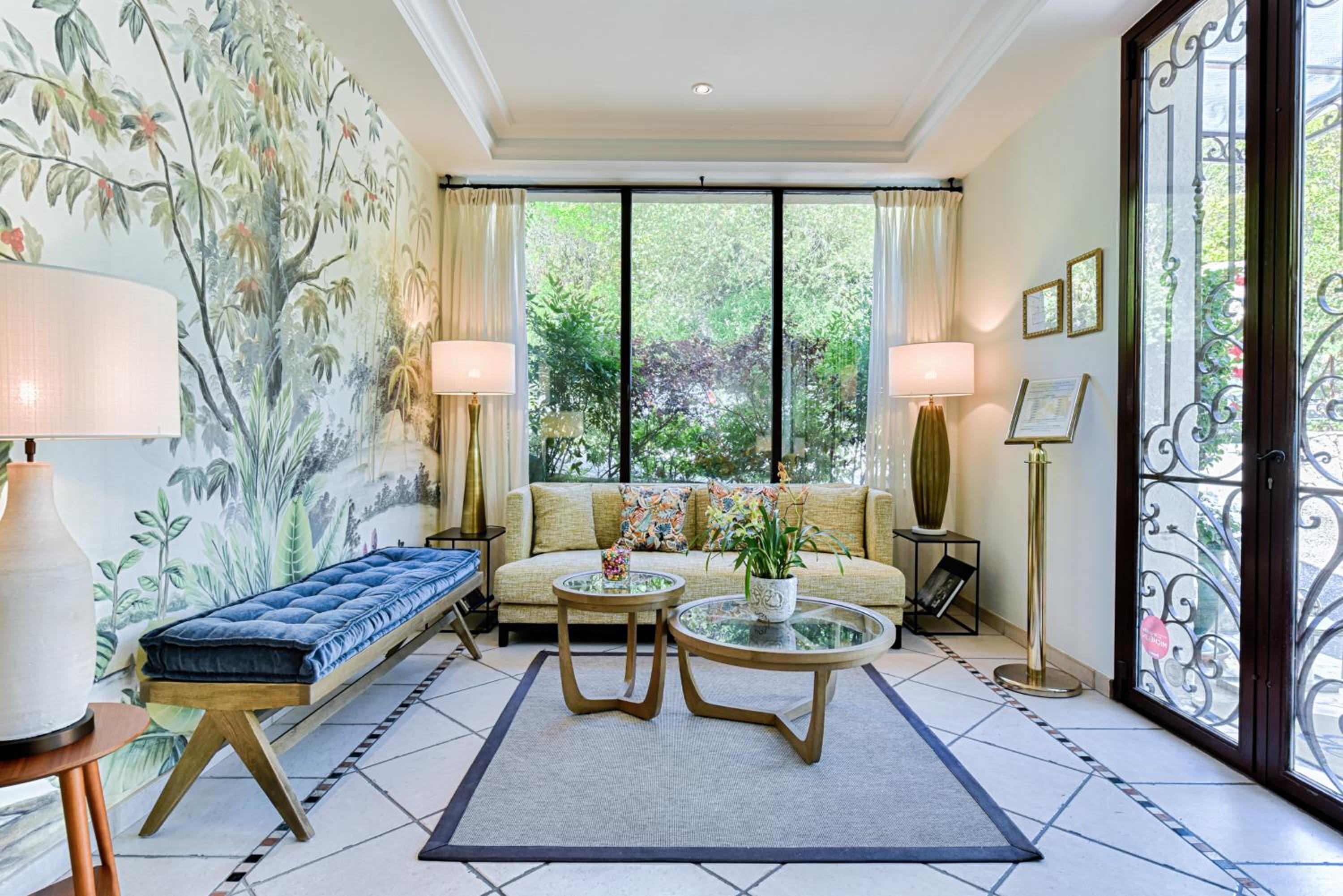 Botanical wallpaper and brass fixtures create an intimate sitting area where French doors frame verdant gardens, inviting quiet moments with morning coffee.