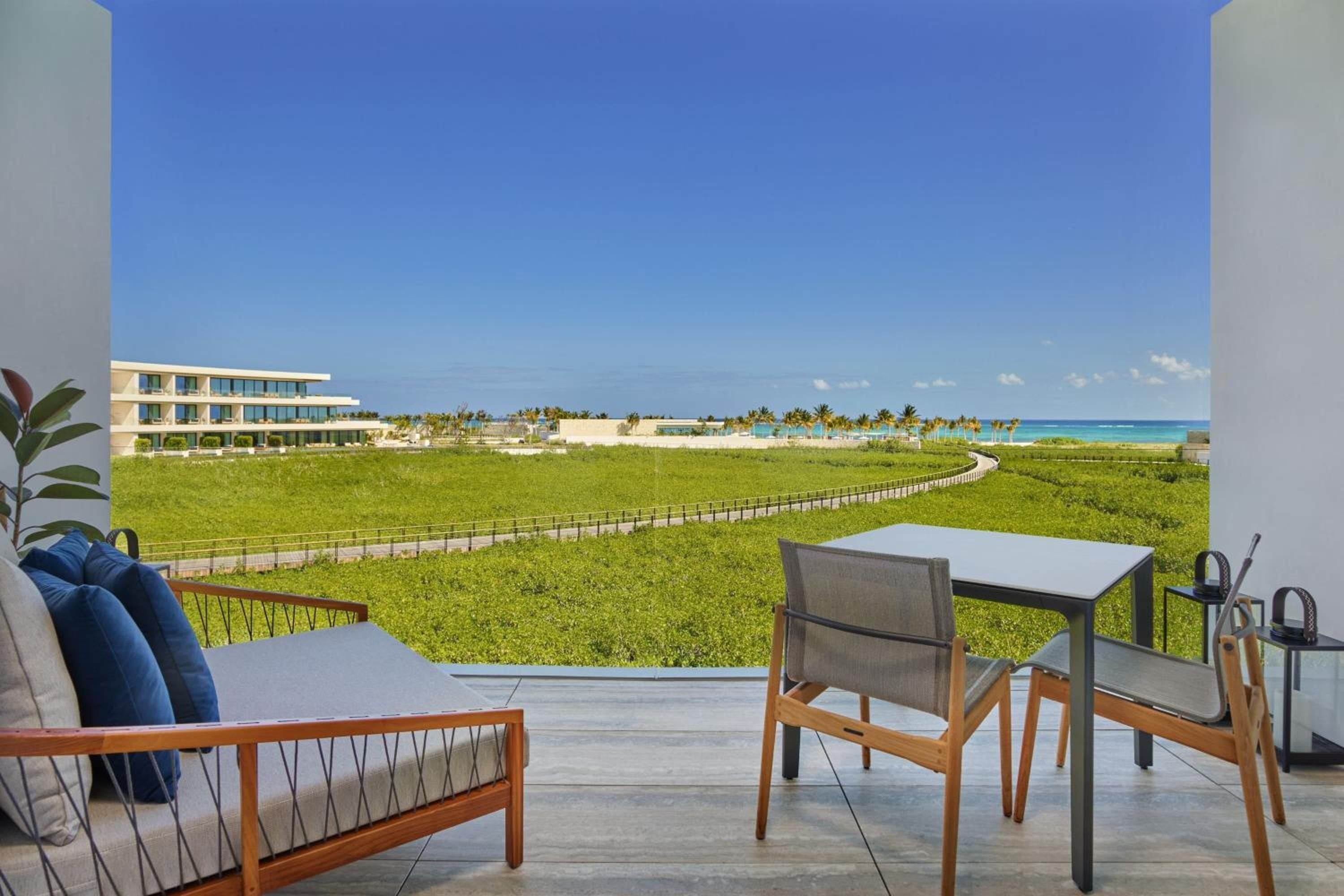 Modern teak furnishings frame sweeping views across emerald mangroves toward the Caribbean, where a winding boardwalk beckons guests into Riviera Maya's pristine coastal wilderness.