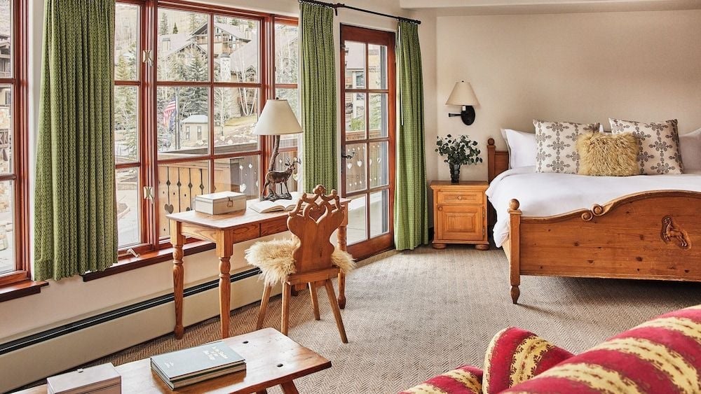 Alpine charm meets refined comfort in guest rooms adorned with hand-carved wooden furnishings, sage green curtains, and cozy sheepskin throws overlooking Park City's mountainside.