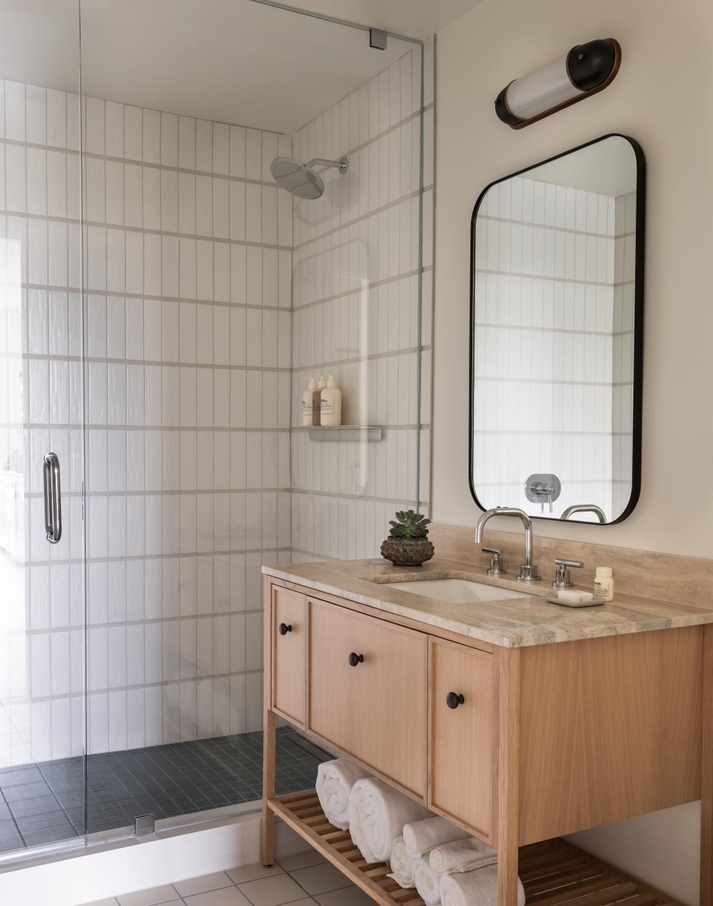 Natural wood vanity meets crisp white subway tile in thoughtfully appointed guest bathrooms, where brass fixtures and clean lines create a modern yet timeless retreat.