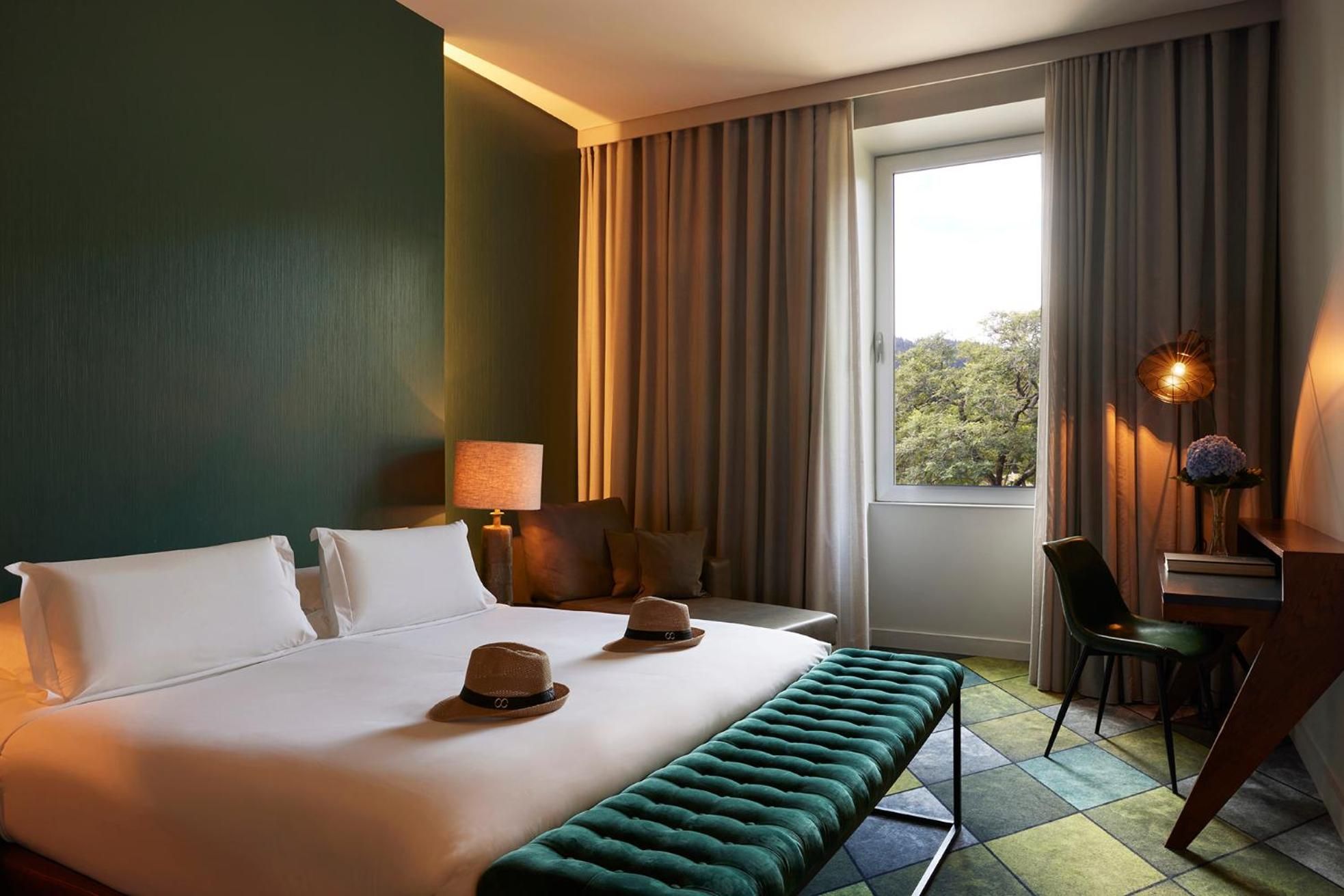 Forest-green walls and warm amber lighting create an intimate cocoon, while geometric carpet patterns in emerald hues ground this sophisticated retreat overlooking verdant Azorean landscapes.