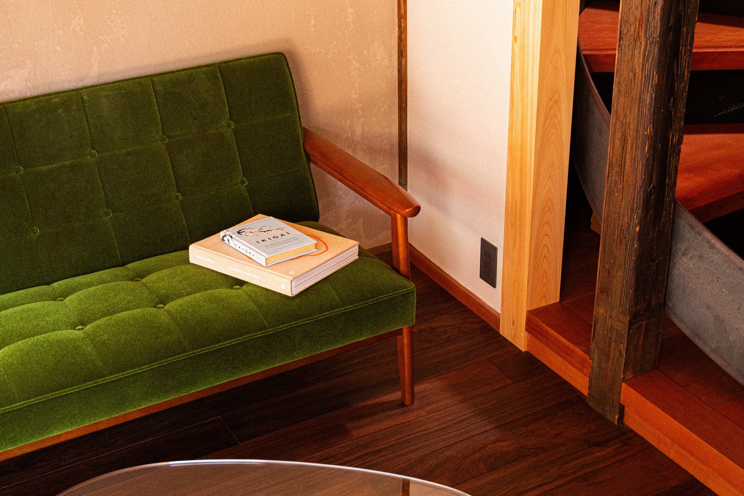 Moss-green velvet upholstery and warm wood tones create an intimate reading nook, where carefully curated books rest beside polished floors and traditional craftsmanship.