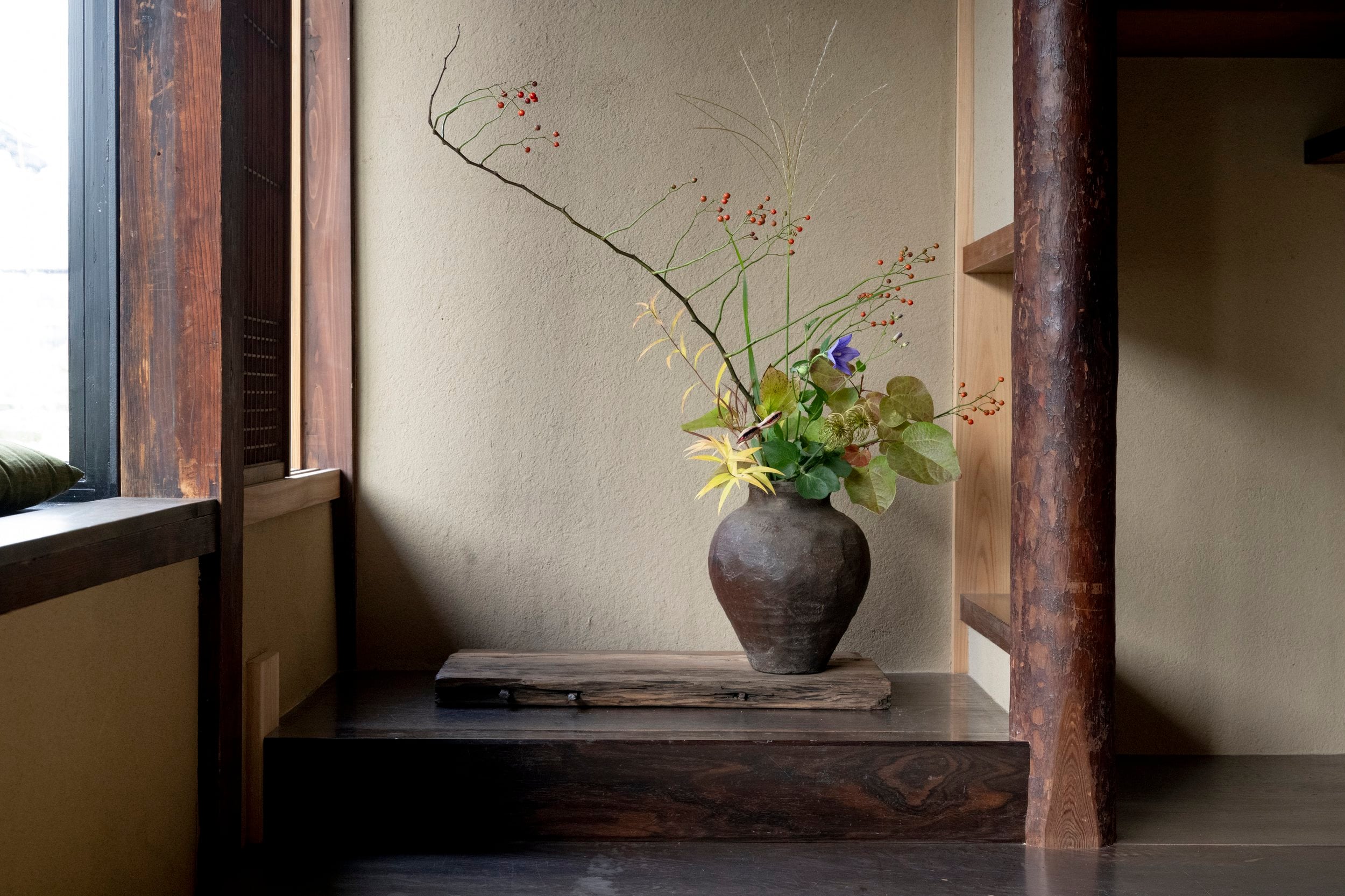Traditional ceramic vessels cradle seasonal ikebana arrangements in a corner alcove, where weathered wood beams and handmade pottery embody Kyoto's enduring craft traditions.