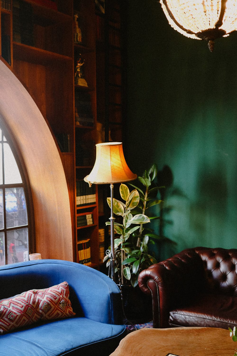 Emerald walls and vintage furnishings create an intimate reading nook, where brass floor lamps cast amber pools of light across plush velvet seating and leather-bound volumes.