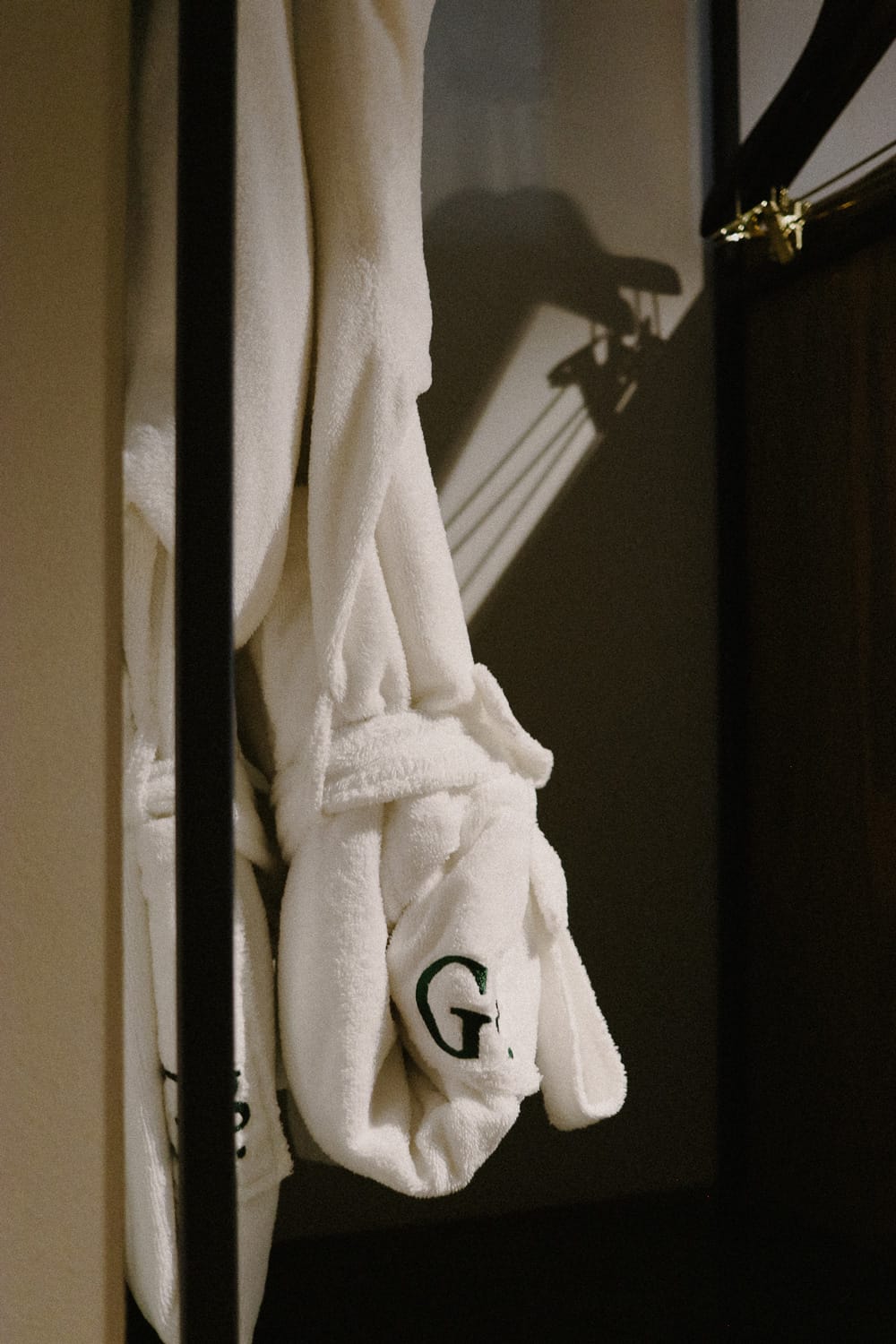 Plush white robes embroidered with the hotel's signature 'G' hang ready in guest quarters, casting gentle shadows against cream-colored walls in the warm evening light.