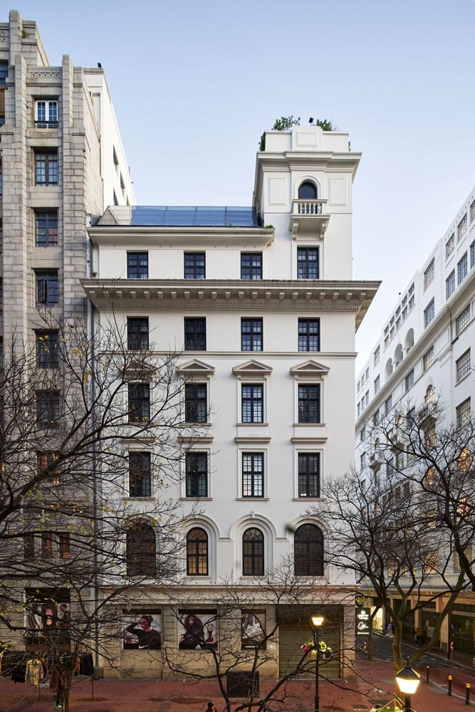 Classical limestone facade rises majestically above bare winter trees, where heritage architecture meets contemporary solar panels and bustling street-level energy below.