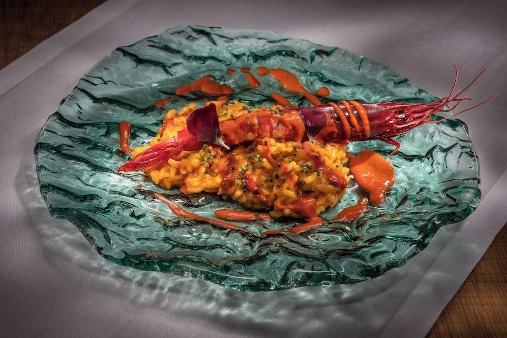 Artfully plated seafood paella arrives on a striking jade-green glass plate, showcasing the hotel's commitment to elevating traditional Spanish cuisine through contemporary presentation.