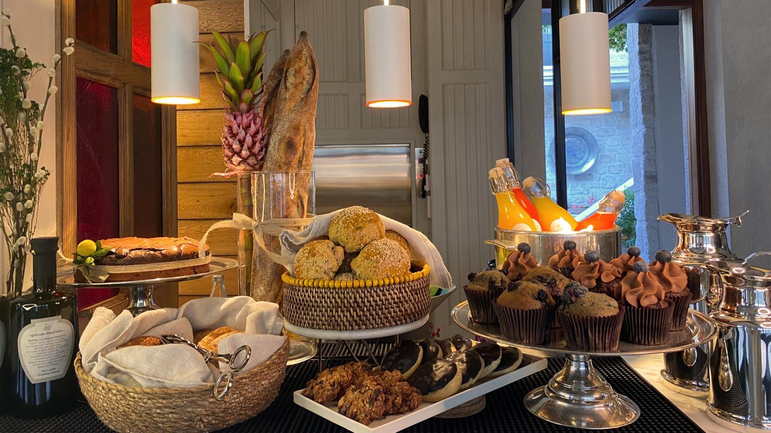 Morning light streams across an artfully arranged breakfast spread, where house-baked breads, seasonal fruits, and chocolate cupcakes invite lingering conversations over coffee.