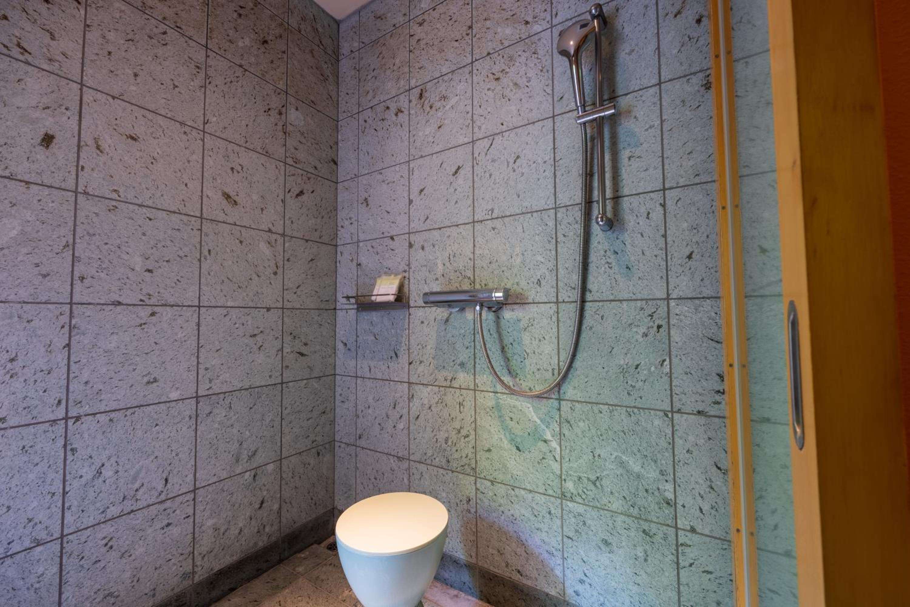 Natural stone tiles with organic speckled patterns create a serene wet room where sleek chrome fixtures complement the earthy, minimalist Japanese aesthetic.