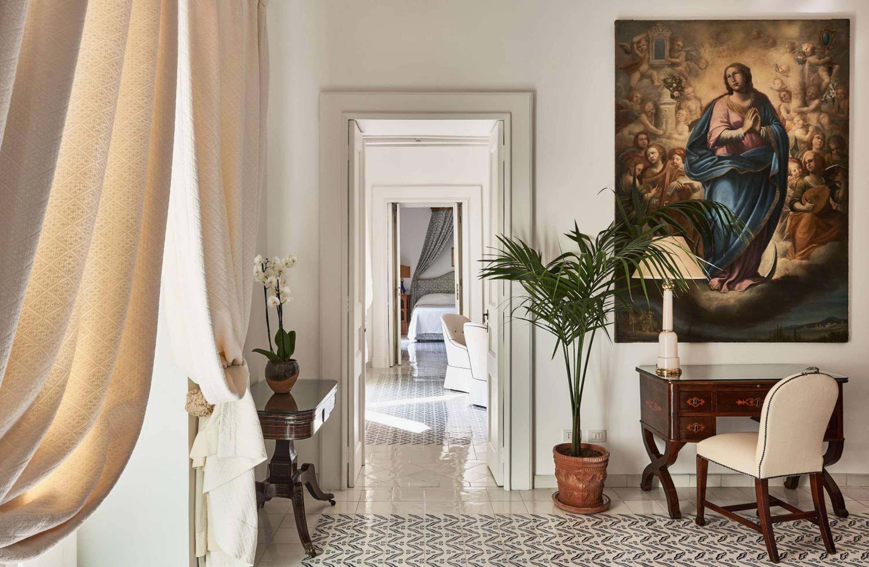 Classical paintings and antique furnishings create an atmosphere of refined elegance, where morning light filters through linen curtains onto gleaming marble floors.