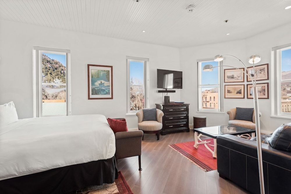 Sunlight streams through floor-to-ceiling windows in this sophisticated suite, where warm hardwood floors meet contemporary furnishings and sweeping mountain vistas frame the Aspen landscape beyond.