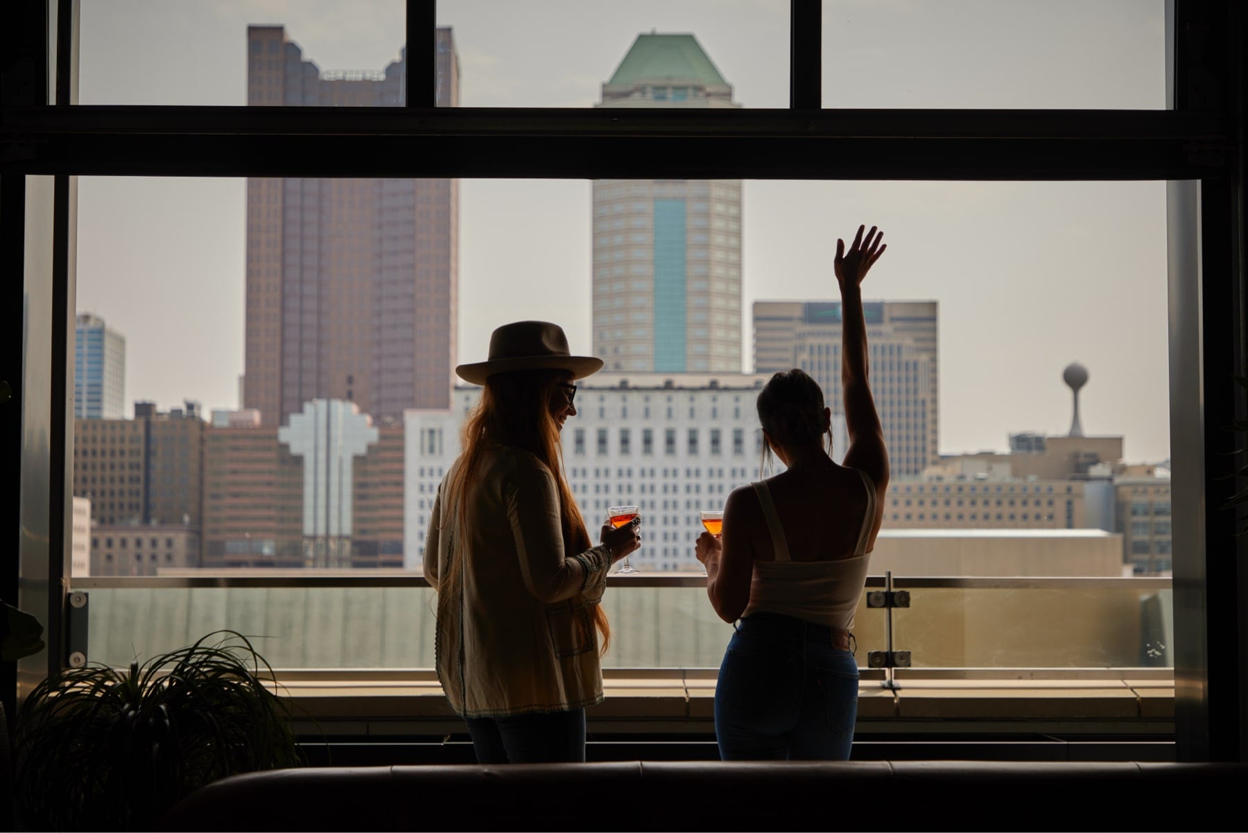 Silhouetted against Dallas's glittering skyline, guests raise their glasses in celebration, golden hour light streaming through floor-to-ceiling windows at this sophisticated urban perch.