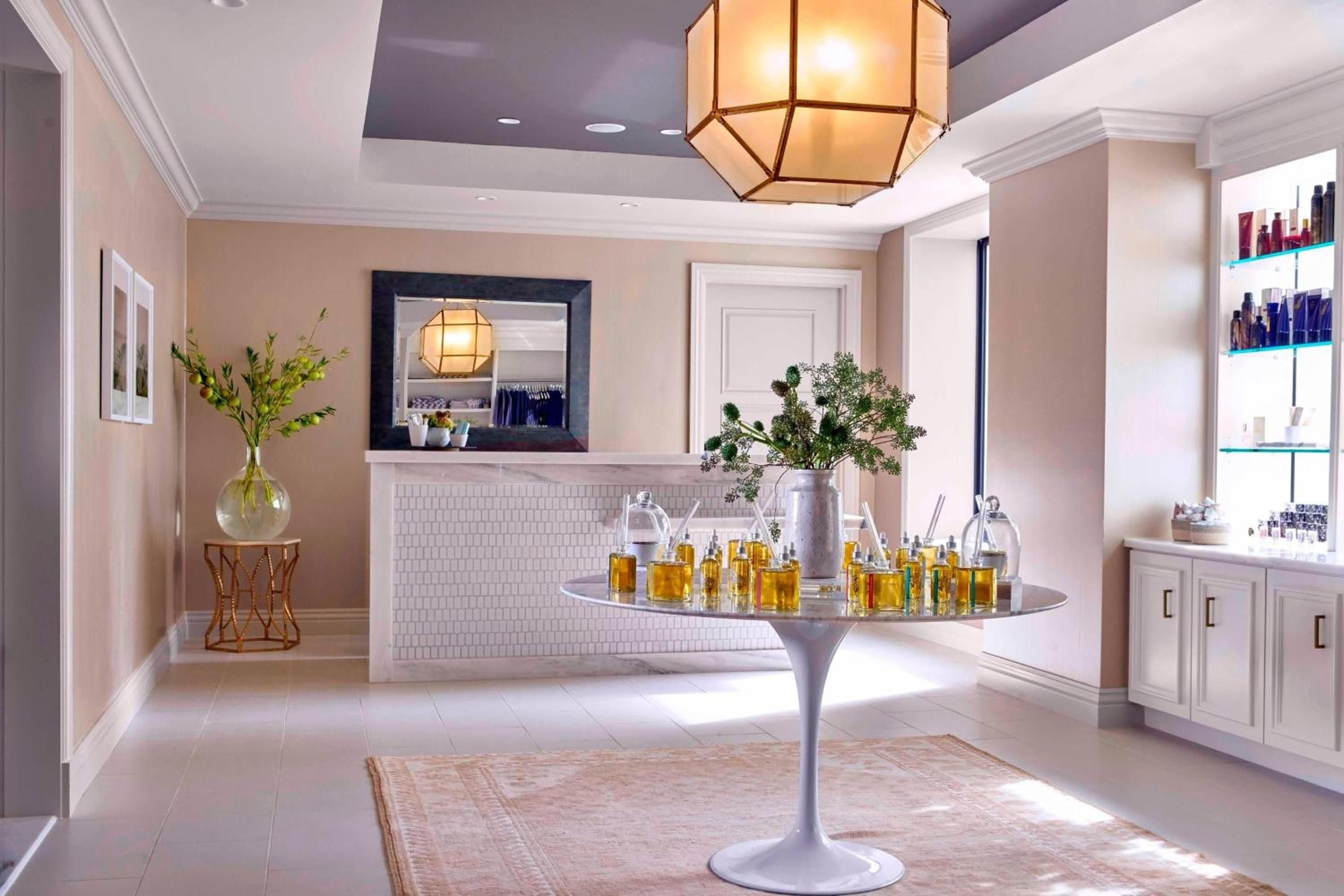 Golden elixirs and botanical essences await on sleek pedestals in this serene treatment sanctuary, where geometric pendant lights cast an amber glow over curated wellness rituals.