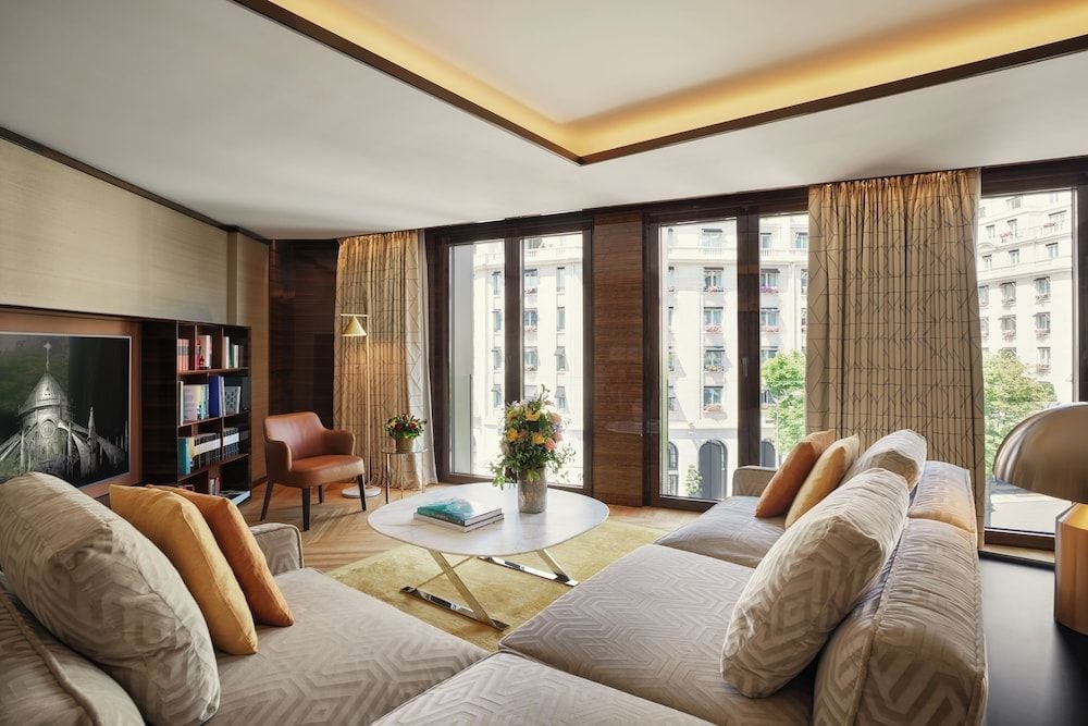 Warm cognac leather and rich walnut paneling create an intimate sanctuary, while floor-to-ceiling windows frame elegant Parisian architecture beyond silk-draped glass.