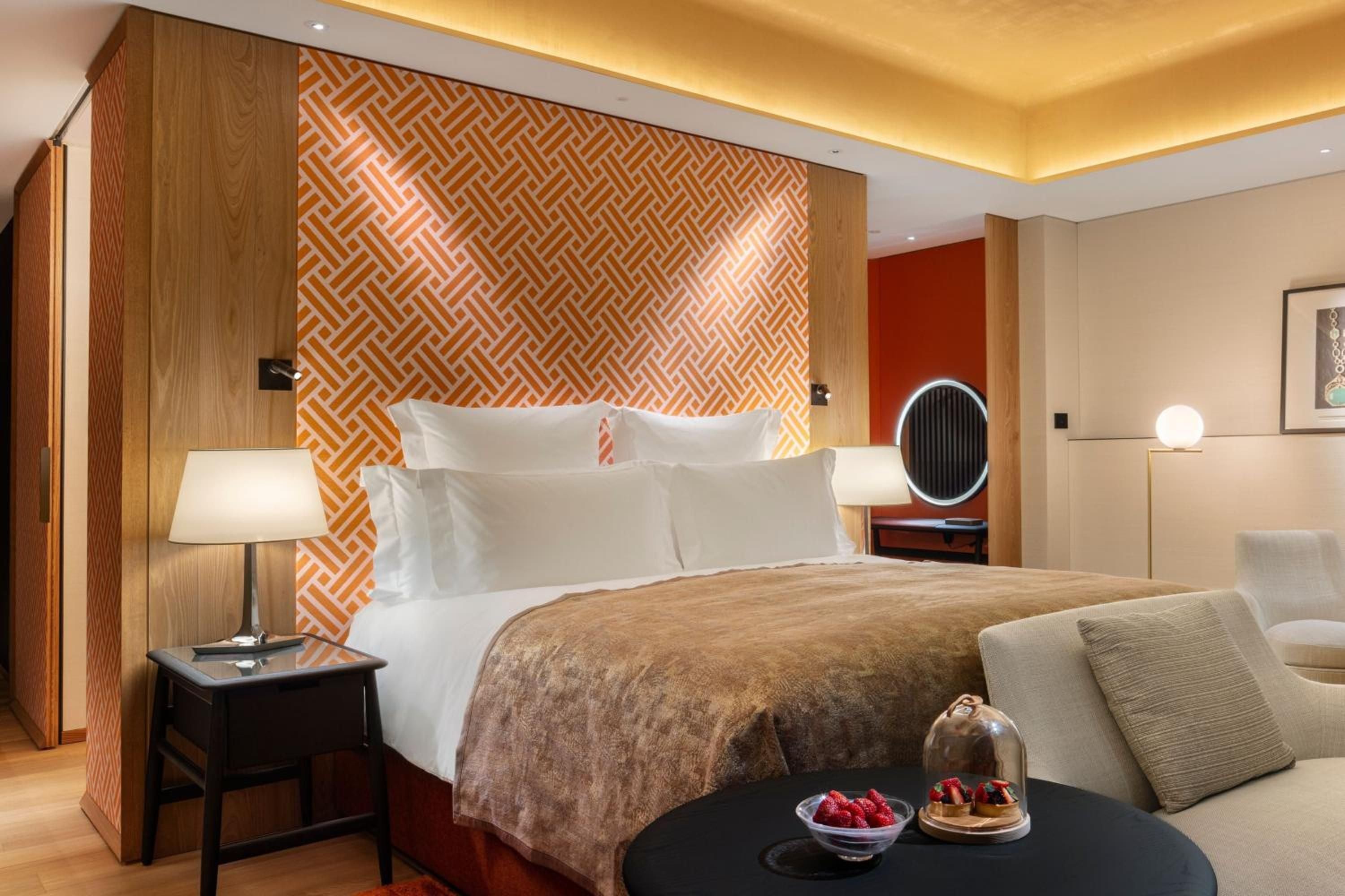 Geometric orange wallpaper creates striking contrast against warm wood paneling, while golden ceiling coves cast an intimate glow over crisp white linens and thoughtful Japanese details.