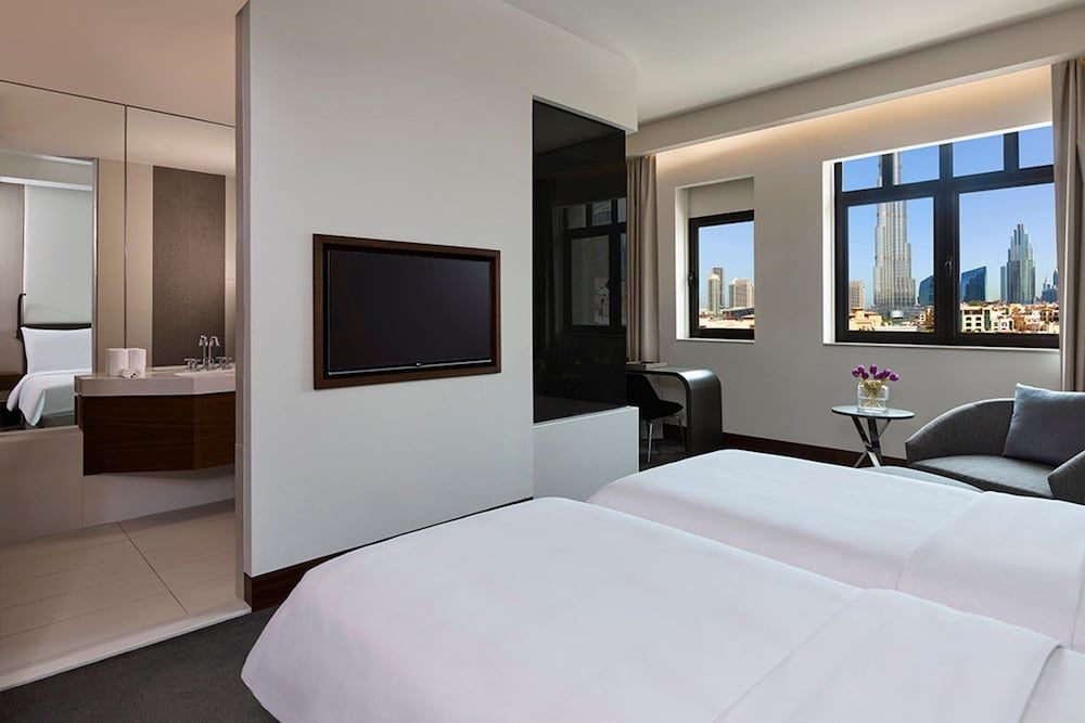 Floor-to-ceiling windows frame Dubai's glittering skyline from this serene suite, where warm wood accents and marble surfaces create an intimate urban sanctuary.