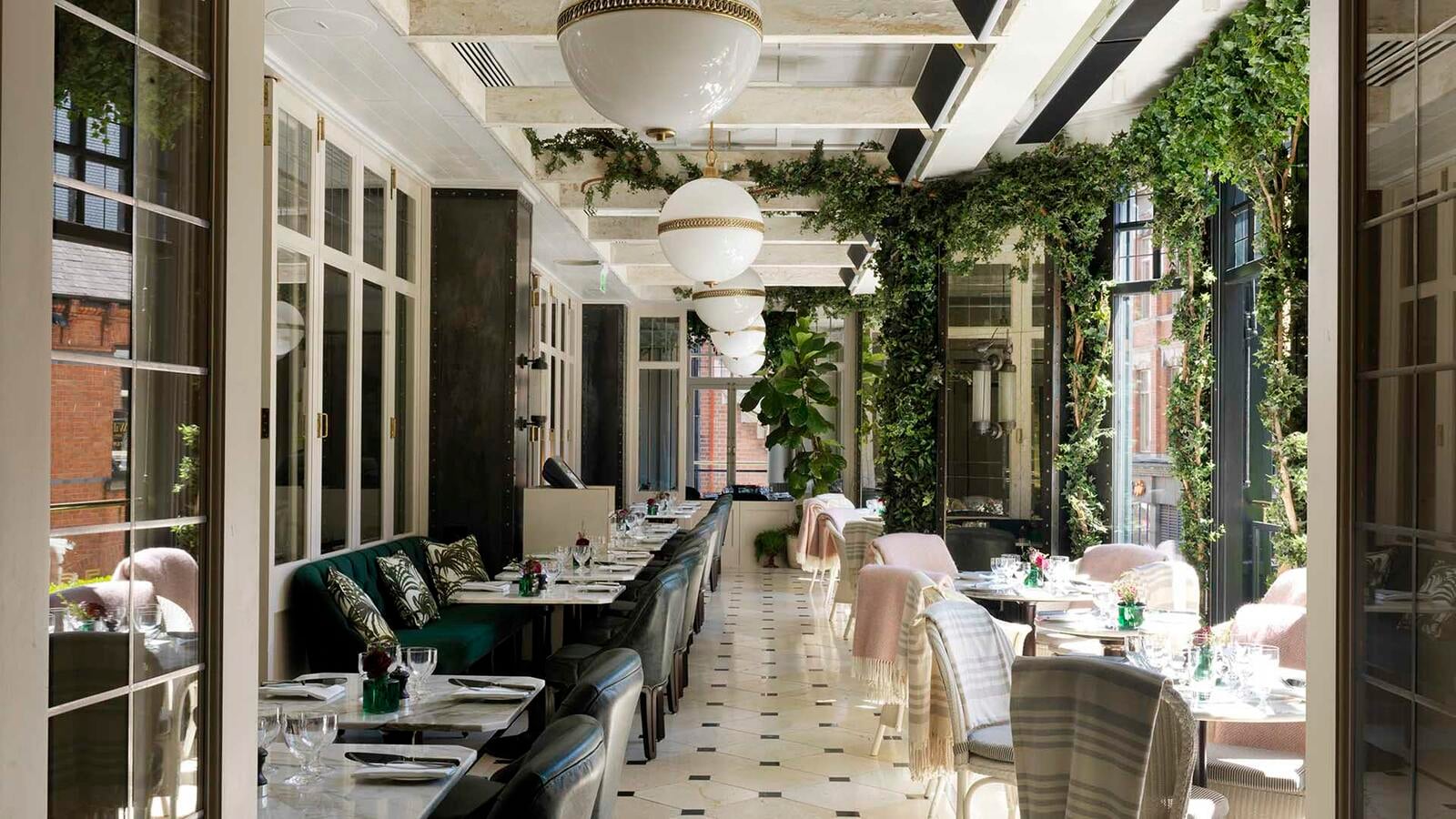 Emerald velvet banquettes and blush-toned chairs create an enchanted garden atmosphere beneath trailing greenery and globe pendant lights in this sophisticated dining sanctuary.