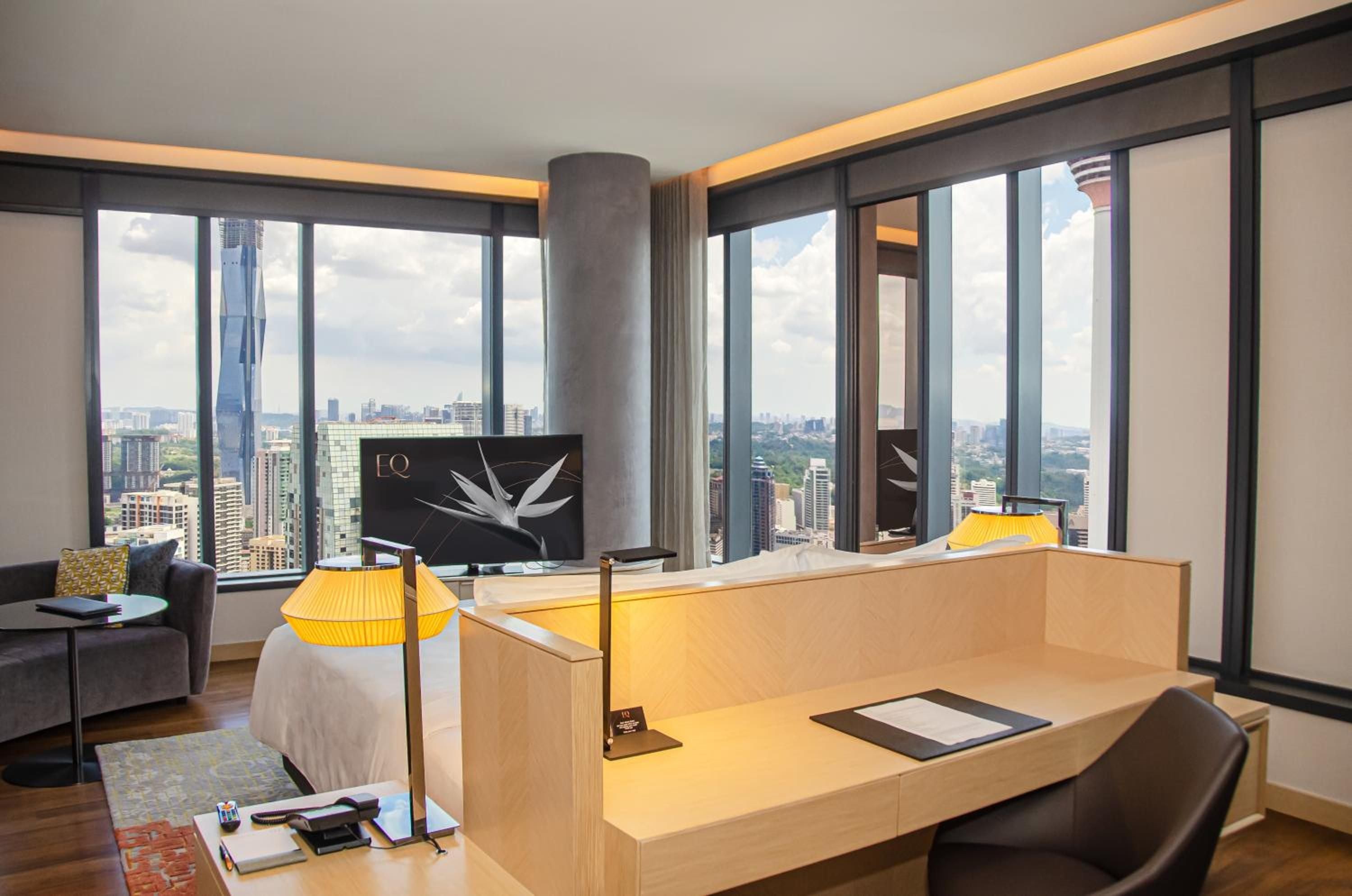 Floor-to-ceiling windows frame Kuala Lumpur's skyline from this contemporary suite, where warm wood furnishings and golden lamplight create an elevated urban sanctuary.