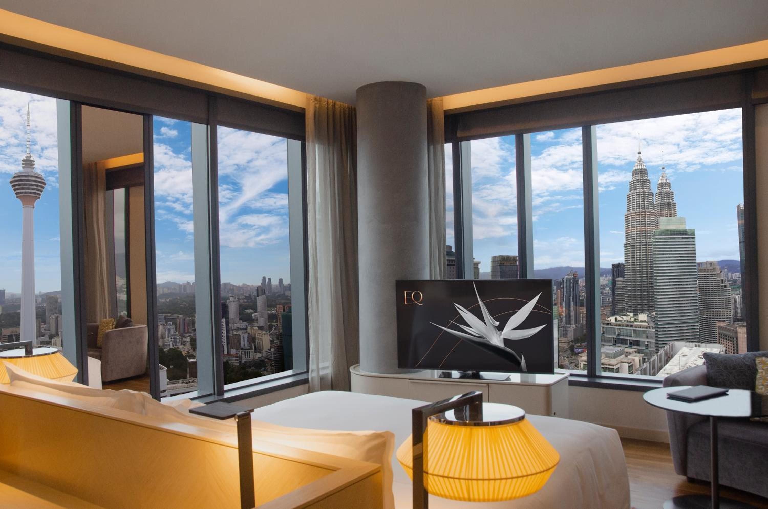 Floor-to-ceiling windows frame Kuala Lumpur's iconic Petronas Towers from this corner suite, where warm wood tones and contemporary furnishings create an elevated urban sanctuary.