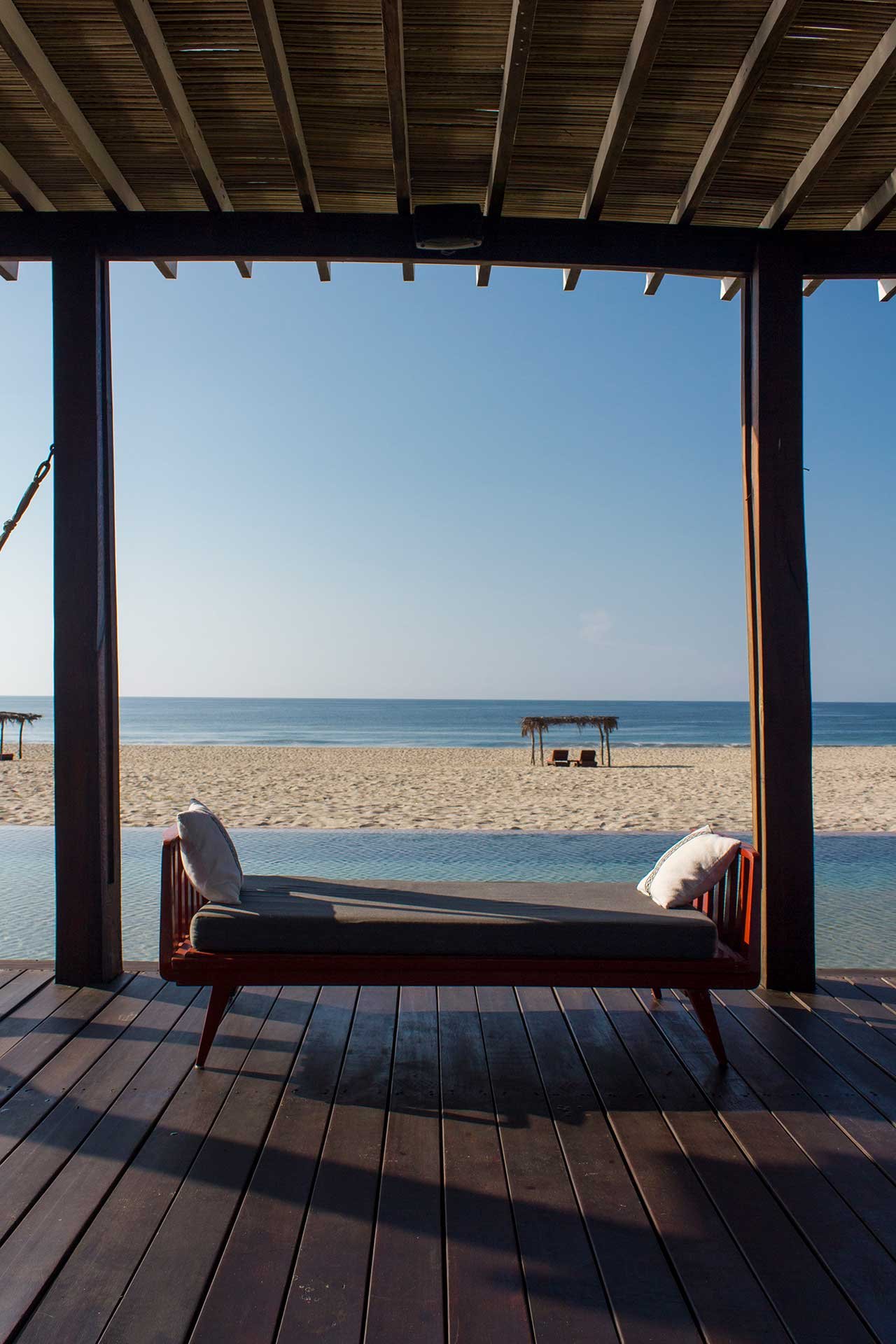 Weathered teak daybed frames an infinity pool that dissolves into Oaxaca's pristine coastline, where golden hour light bathes sand and endless blue horizon.
