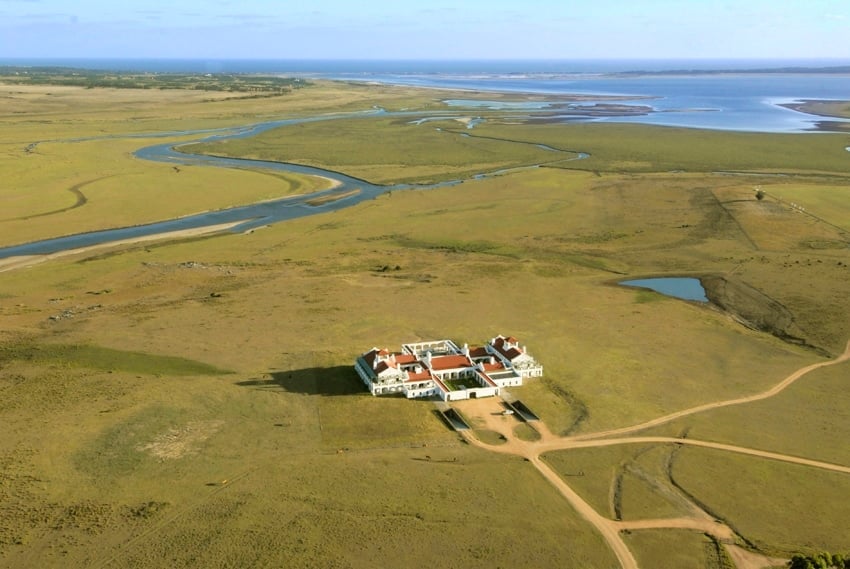 Remote splendor unfolds across Uruguay's windswept pampas, where this striking estancia sits like a white jewel amid endless golden grasslands and serpentine waterways.