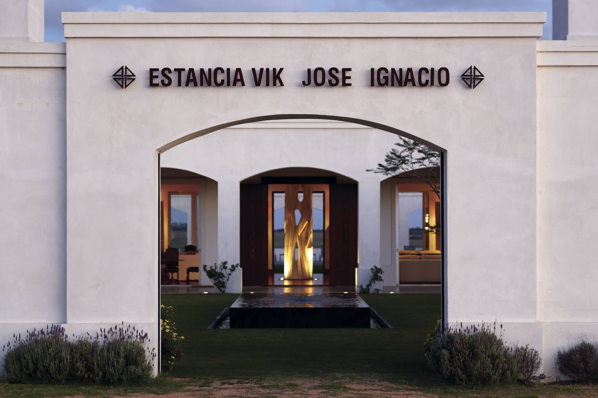 Softly illuminated stone archways frame the estate's welcoming entrance, where contemporary sculpture and manicured lavender create an elegant threshold between countryside and refined hospitality.