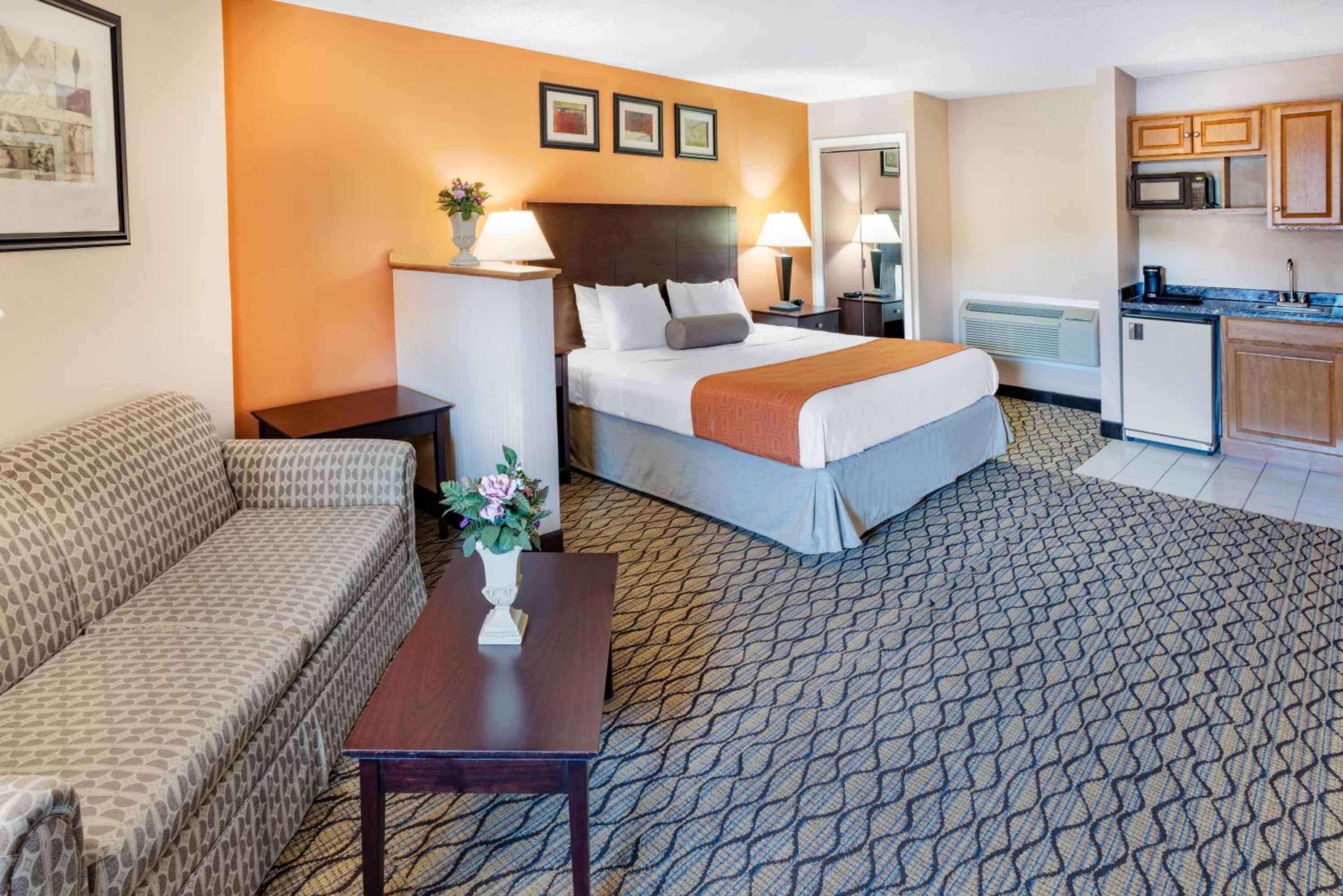 Warm orange accent walls and geometric carpeting create a welcoming extended-stay suite, complete with kitchenette and separate seating area for longer getaways.