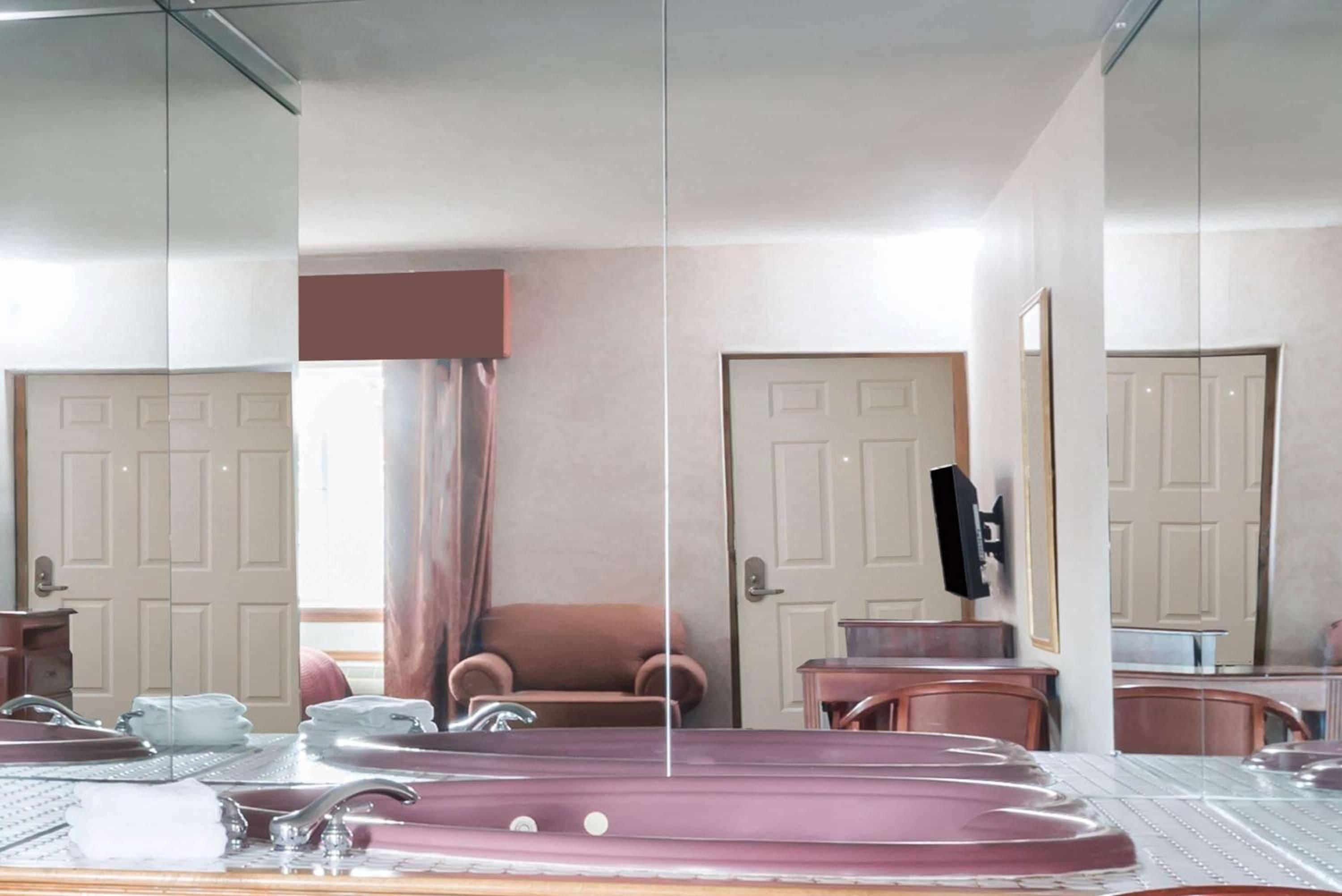Mirrored walls amplify natural light in this luxurious bathroom, where a deep soaking tub overlooks elegant furnishings and classic paneled doors beyond.