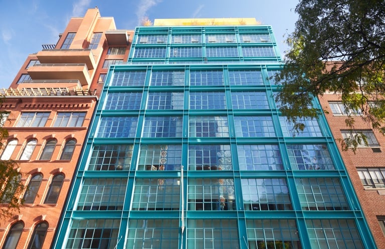 Contemporary glass and steel architecture creates striking contrast against neighboring historic brick buildings, showcasing the hotel's modern presence in Manhattan's diverse streetscape.