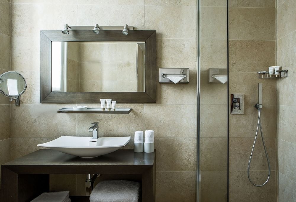Warm limestone tiles and sleek fixtures create a spa-like sanctuary where modern vessel sinks meet timeless French elegance in perfectly curated silence.