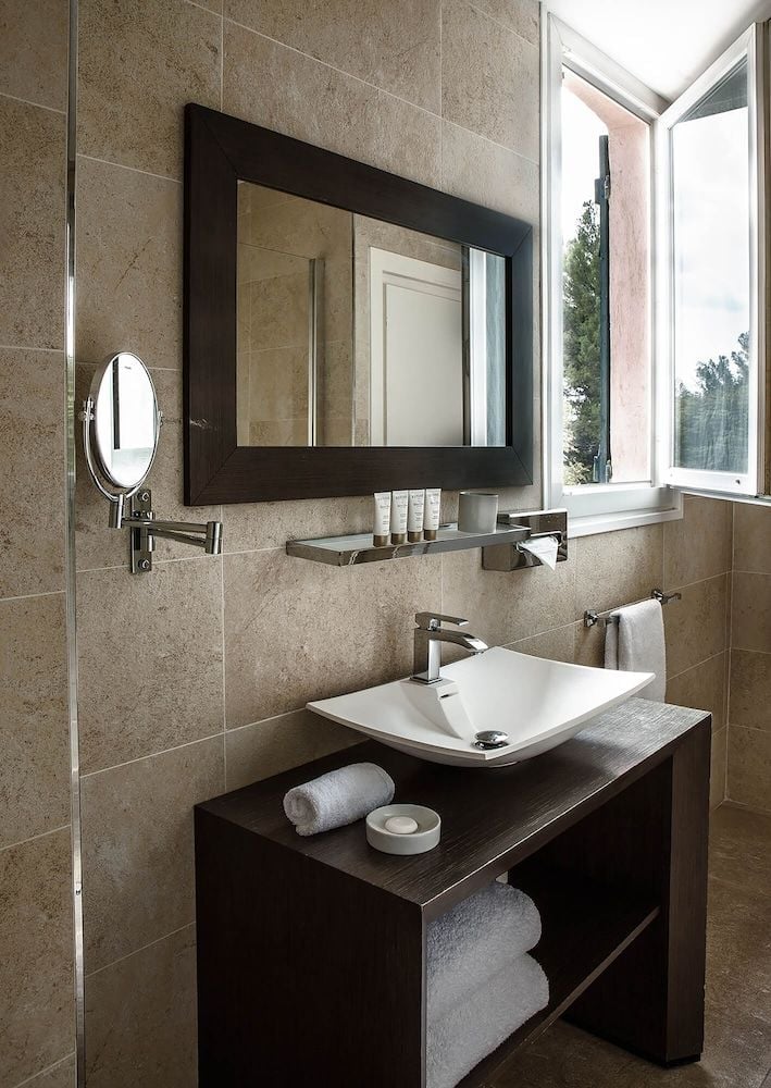 Natural stone tiles and dark wood vanities create a spa-like sanctuary where modern fixtures complement the hotel's Provençal elegance and attention to craftsmanship.