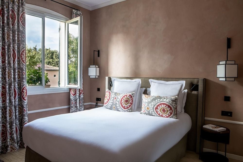Warm terracotta walls create an intimate cocoon in this elegant guest room, where geometric-patterned pillows add Mediterranean flair to crisp white linens and modern pendant lighting.