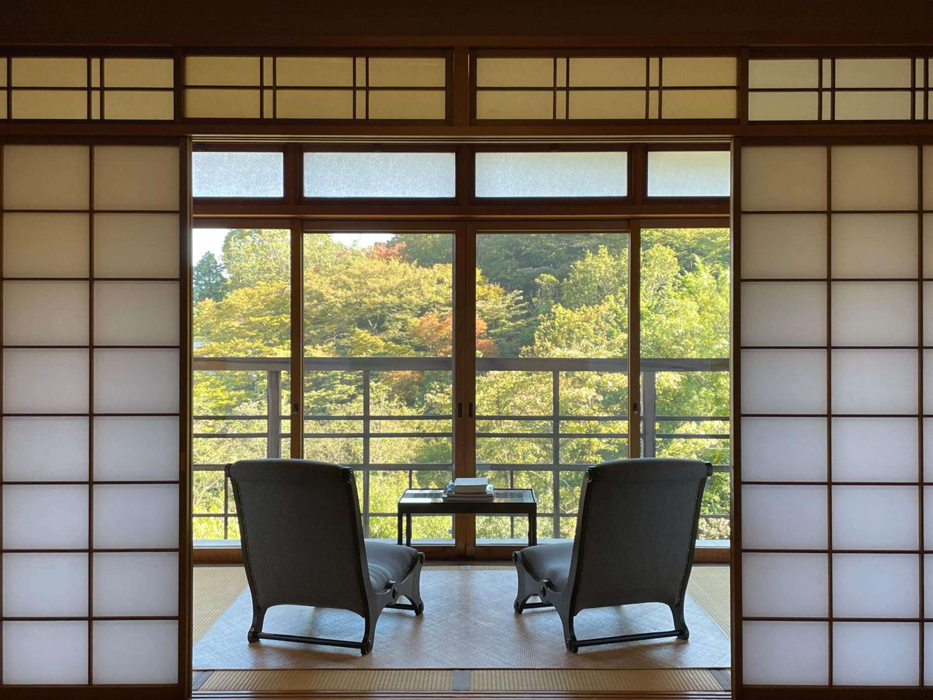 Traditional shoji screens frame an intimate tatami seating area where autumn foliage creates a living painting beyond latticed windows, embodying Japanese minimalist elegance.