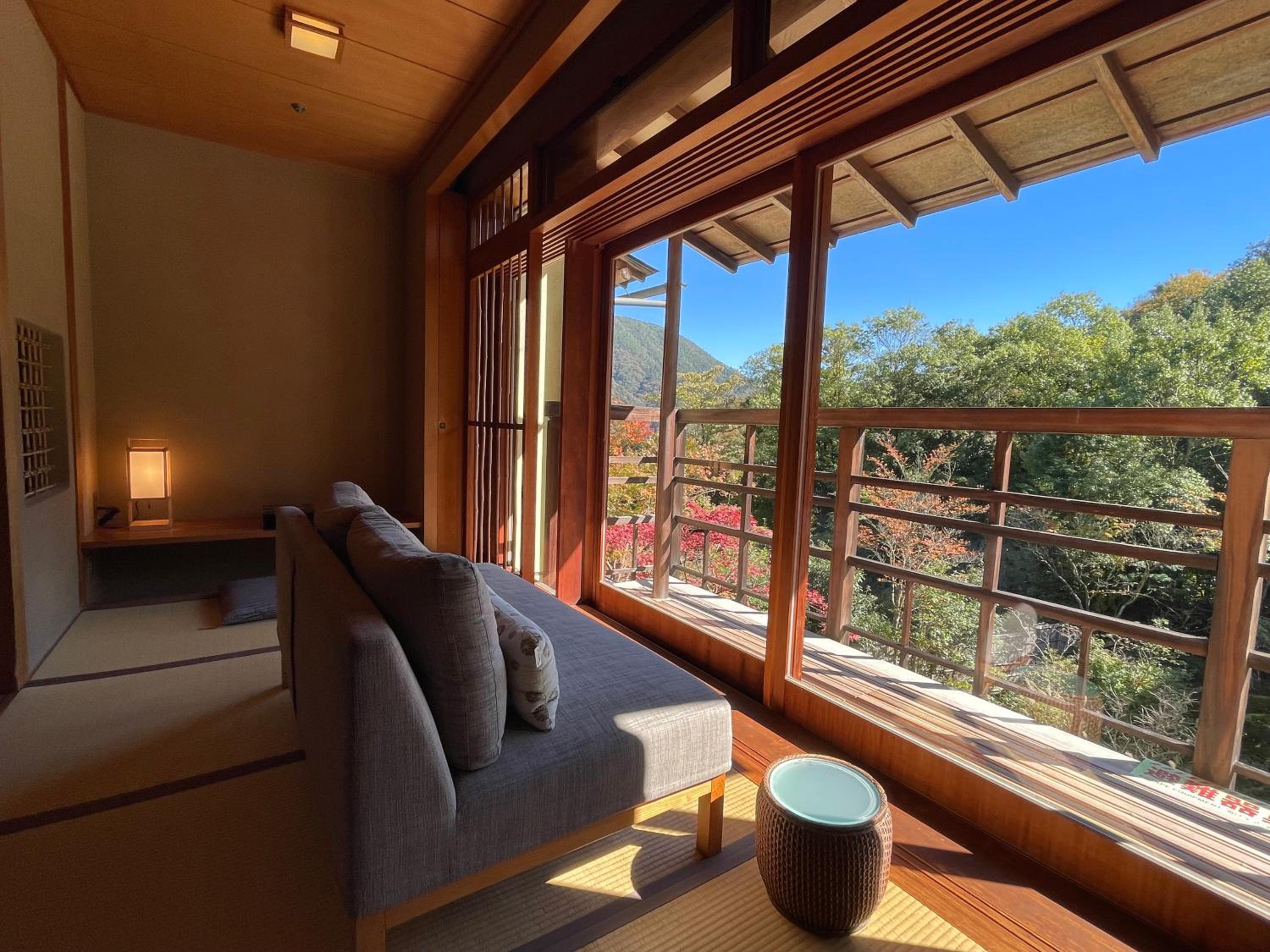 Warm tatami floors and floor-to-ceiling windows frame autumn foliage views from this serene Japanese suite, where modern comfort meets traditional design.
