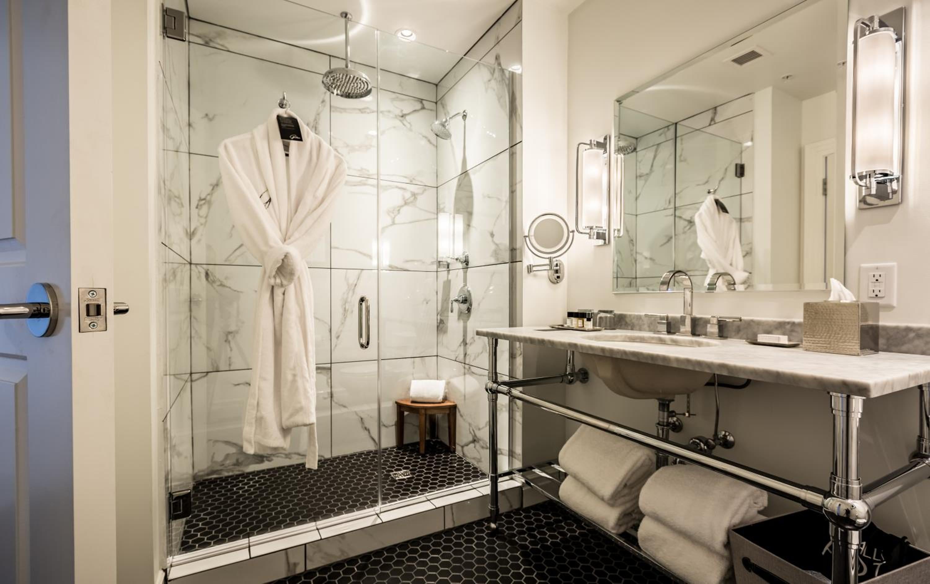 Carrara marble walls and rainfall showers create a spa-like sanctuary, while plush robes and hexagonal penny tiles add thoughtful luxury touches throughout this serene retreat.