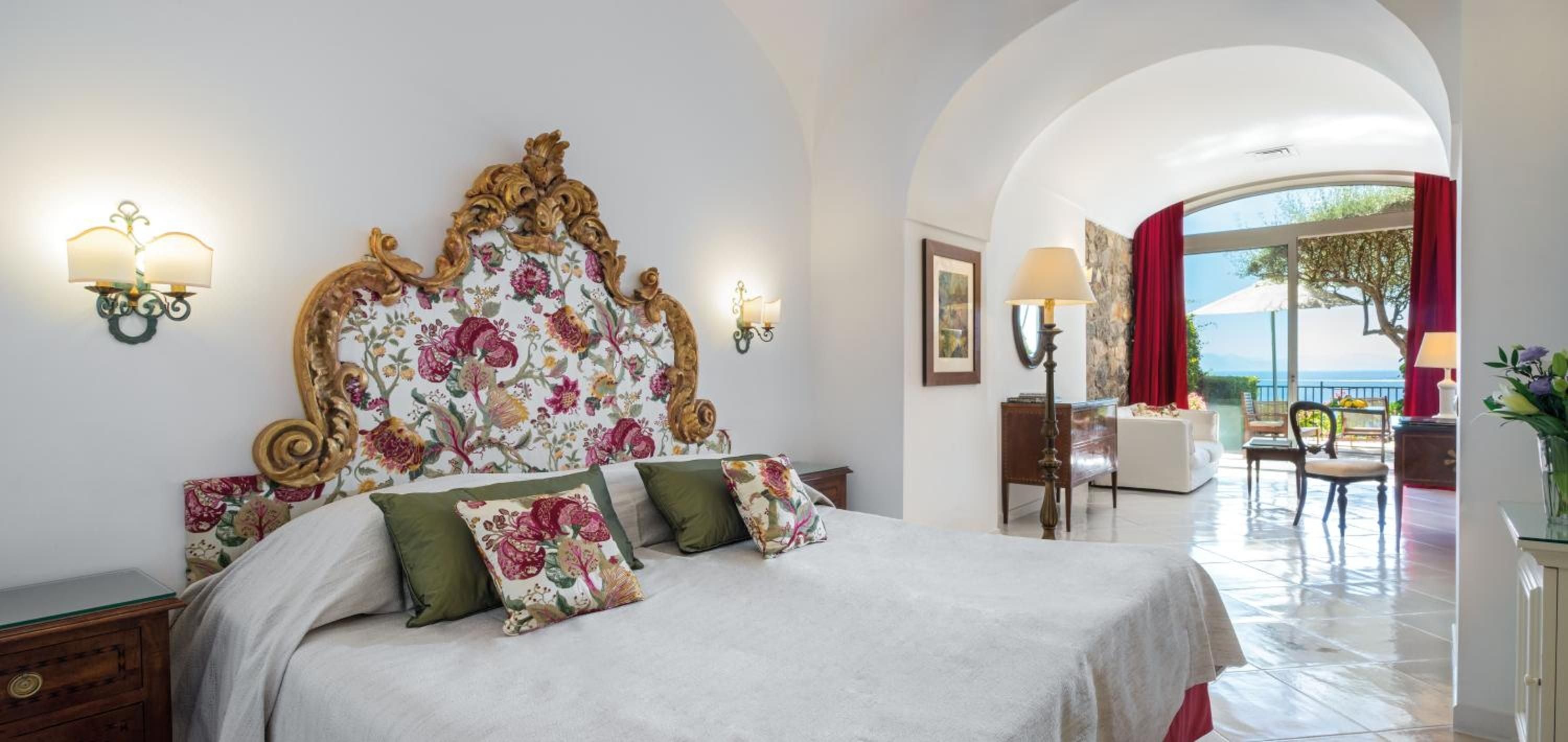 Ornate gilded headboard with floral upholstery commands this elegant suite, where arched ceilings and marble floors create an atmosphere of refined Mediterranean luxury.