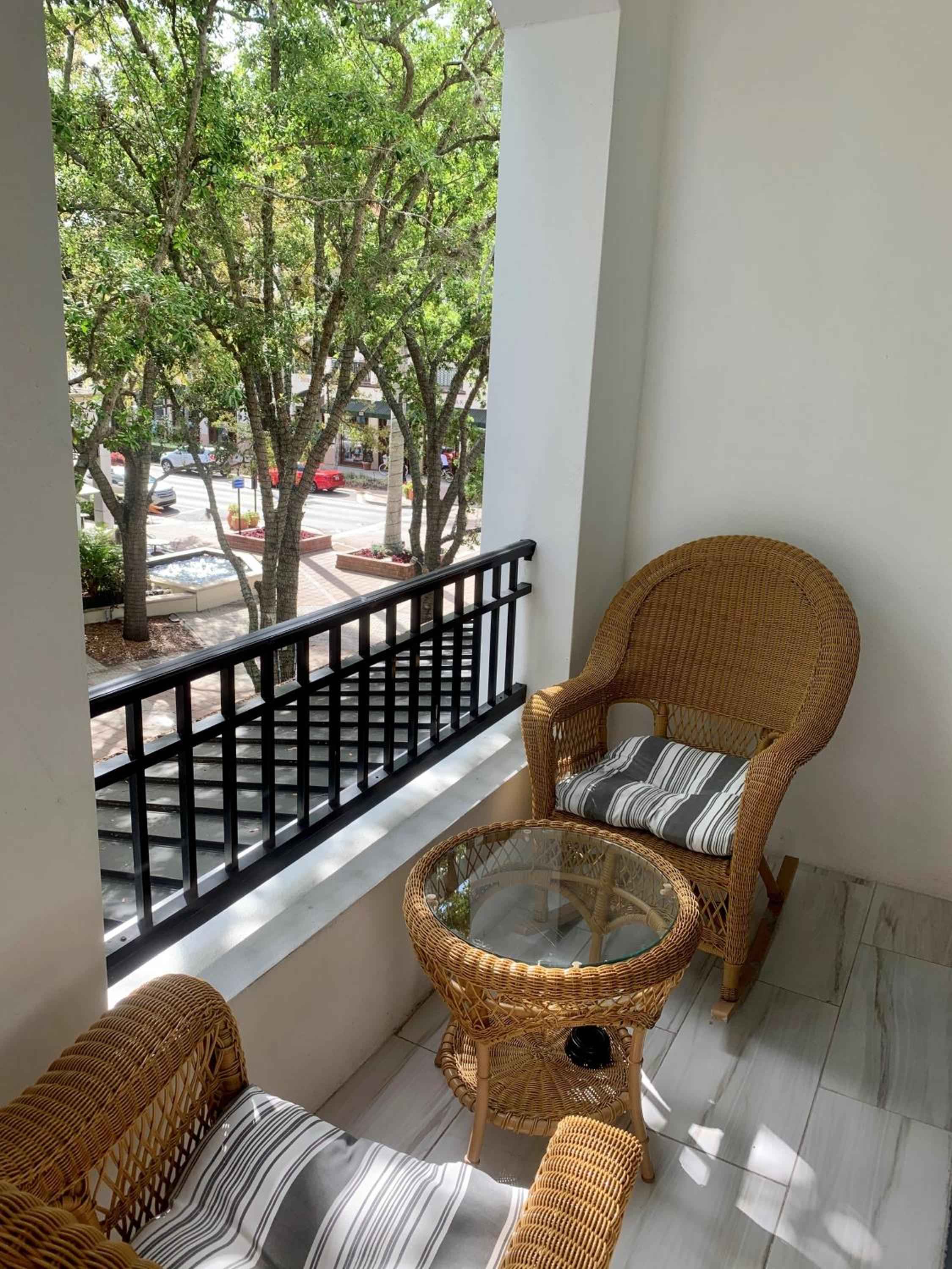 Wicker furniture creates an intimate retreat on this private balcony, where dappled sunlight filters through lush canopy trees overlooking Naples' charming streetscape below.