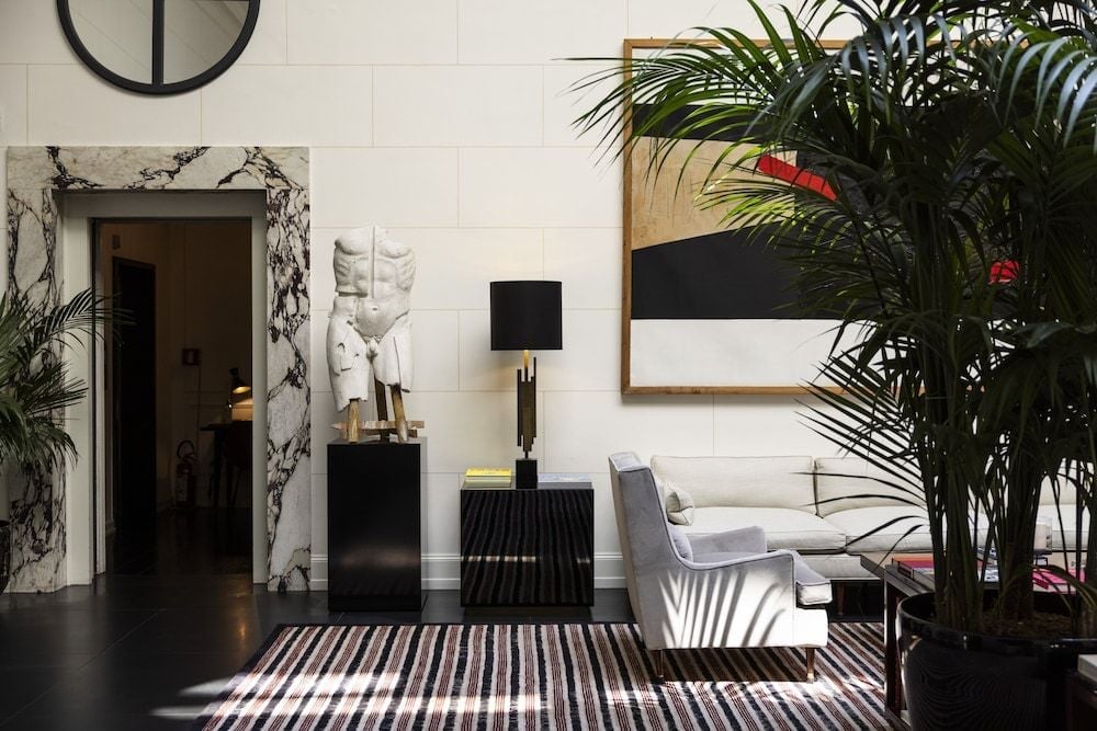 Marble doorways frame intimate seating vignettes where contemporary art meets classical sculpture, while towering palms cast dramatic shadows across polished floors.