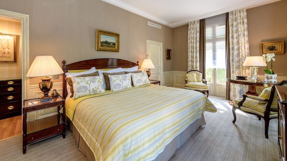 Elegant four-poster mahogany bed anchors this refined guest room, where soft yellow linens complement warm taupe walls and period furnishings create timeless French sophistication.